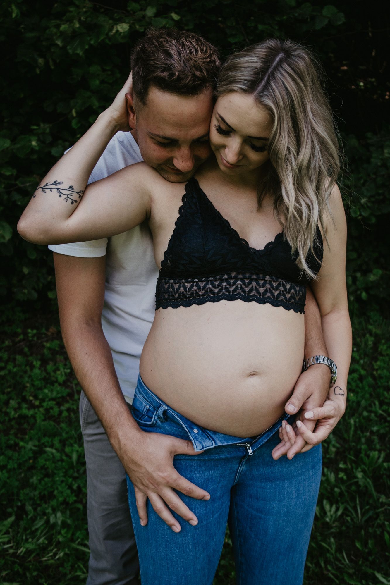 Loving couple embracing during outdoor maternity photoshoot in casual attire.
