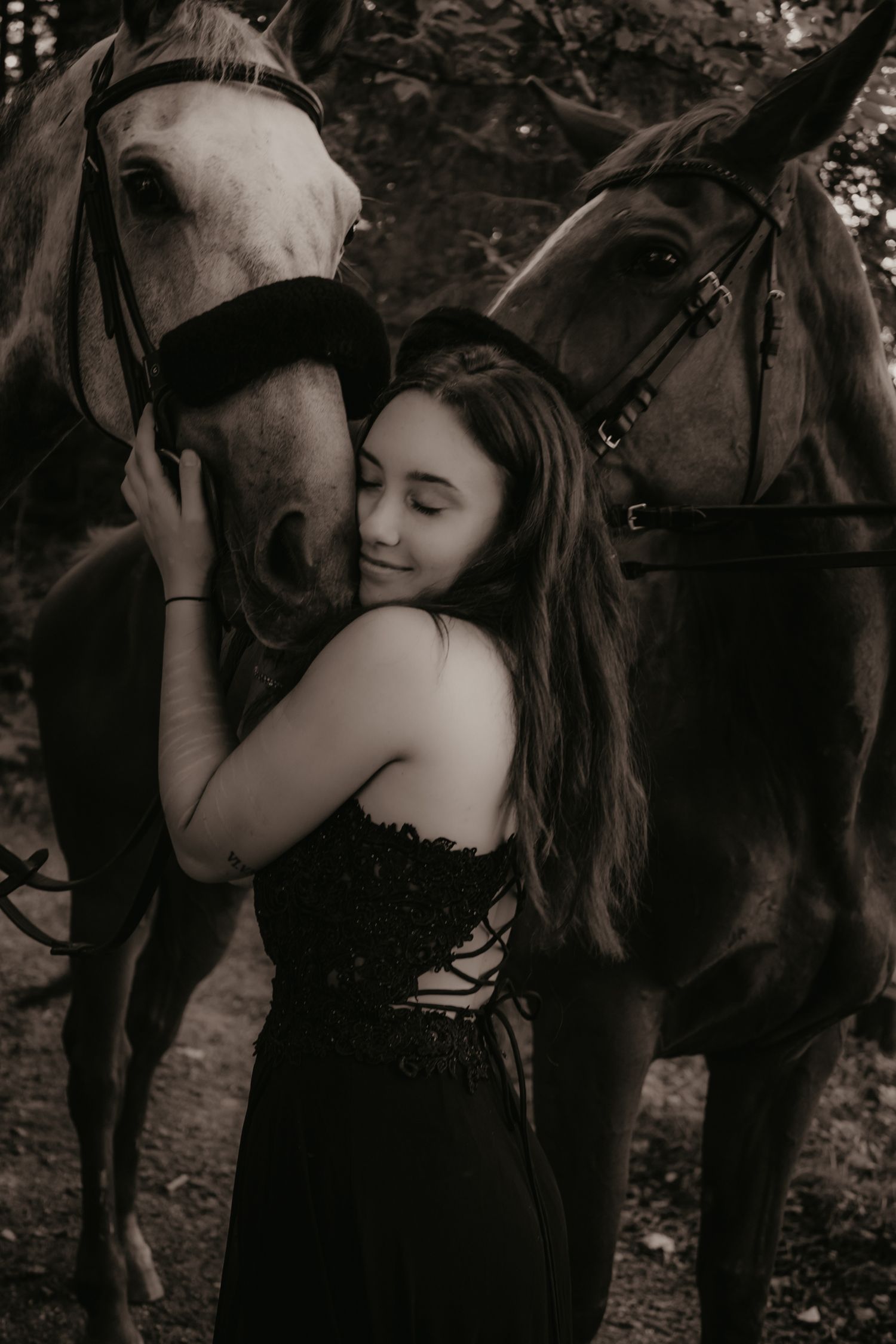 A tender black and white portrait with two horses in a forest setting.