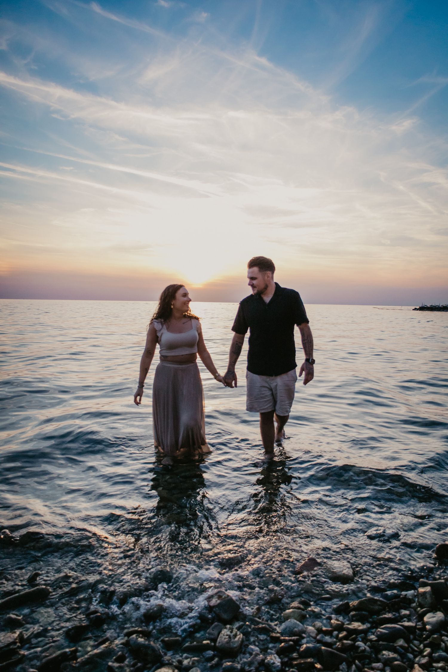 A couple wades through ocean water together during a beautiful sunset.
