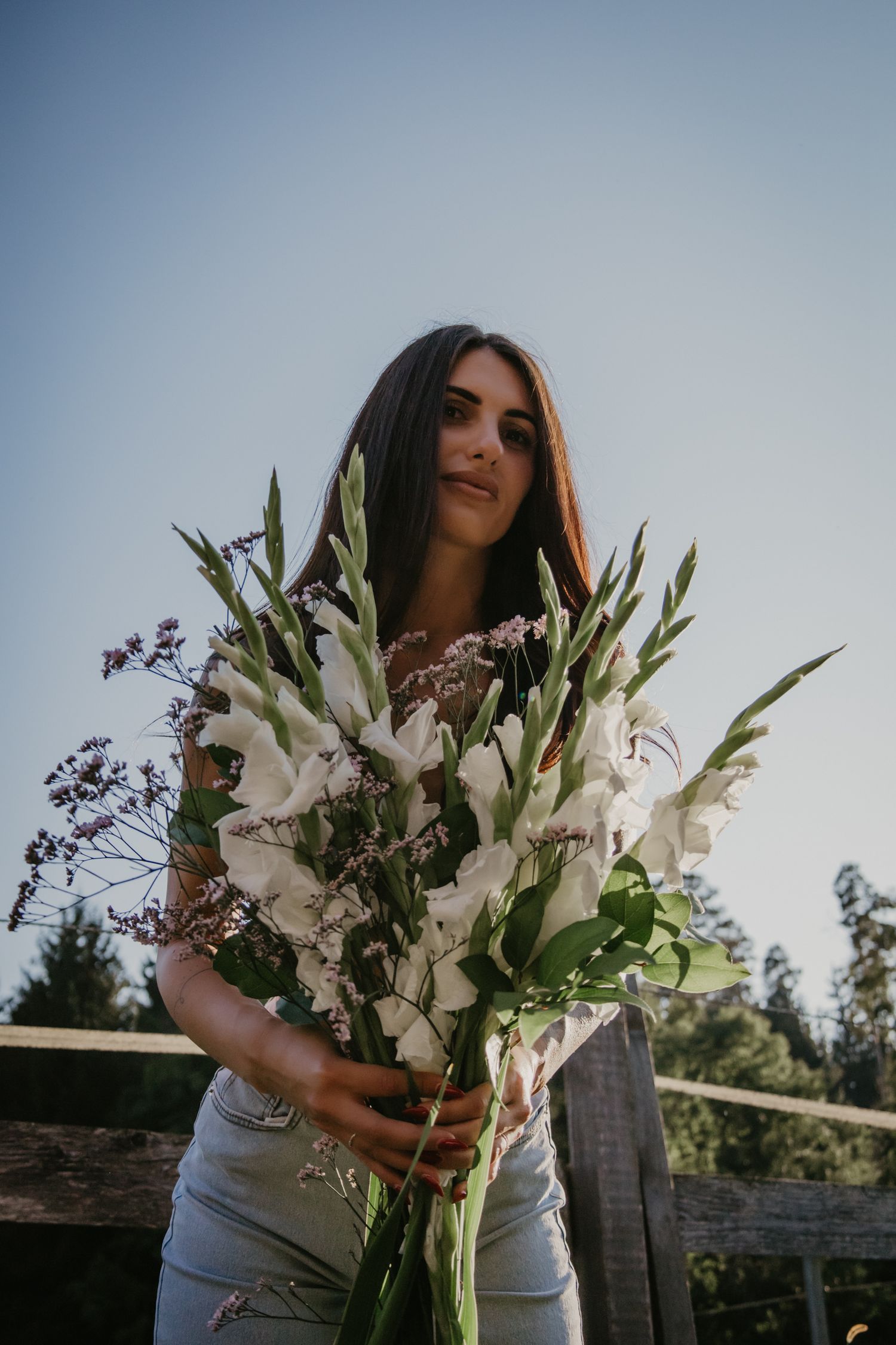 Ethereal portrait with large white flower bouquet against evening sky and rustic fence.