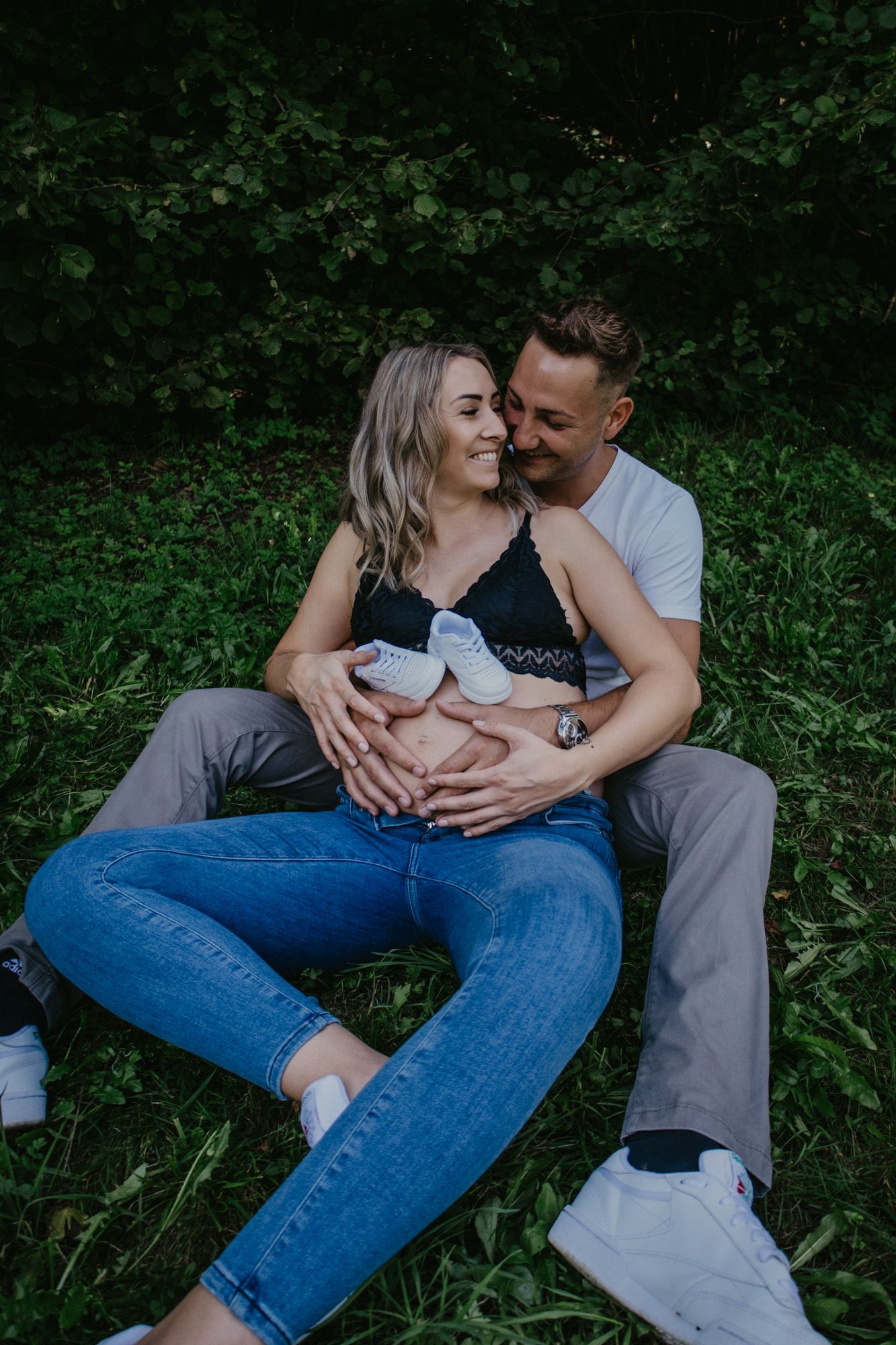 A couple sits together on grass sharing tender moments.
