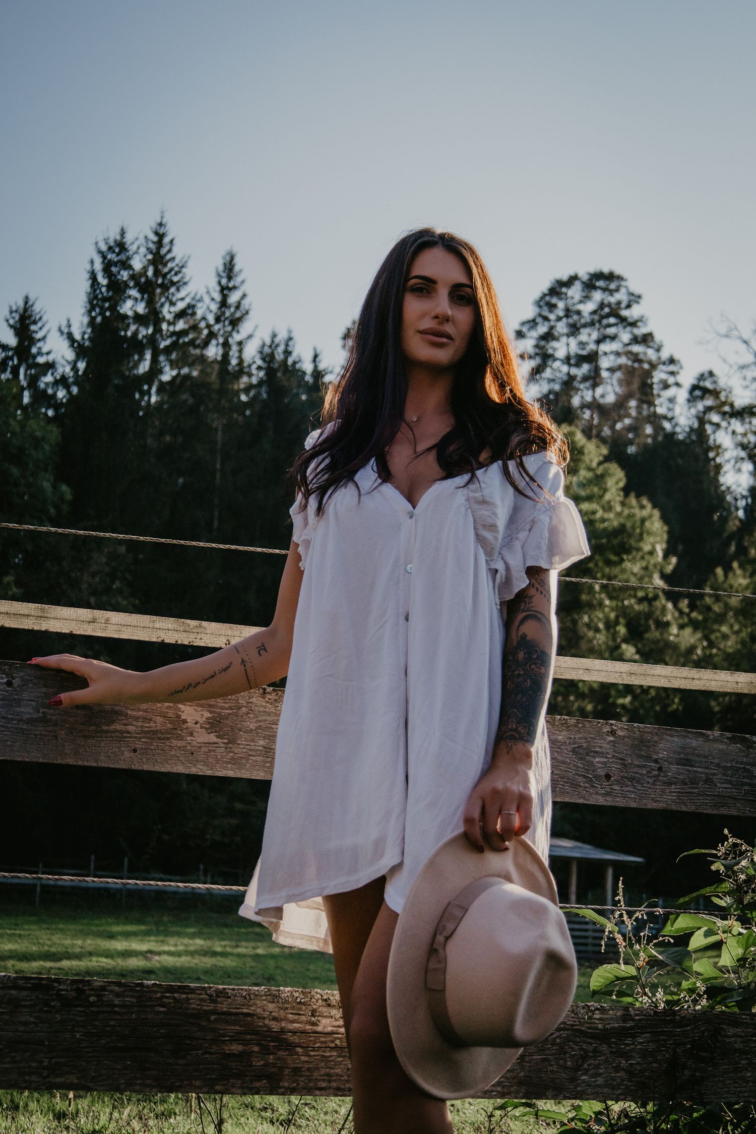 A dreamy outdoor photoshoot featuring a white flowy dress and rustic wooden fence at golden hour.