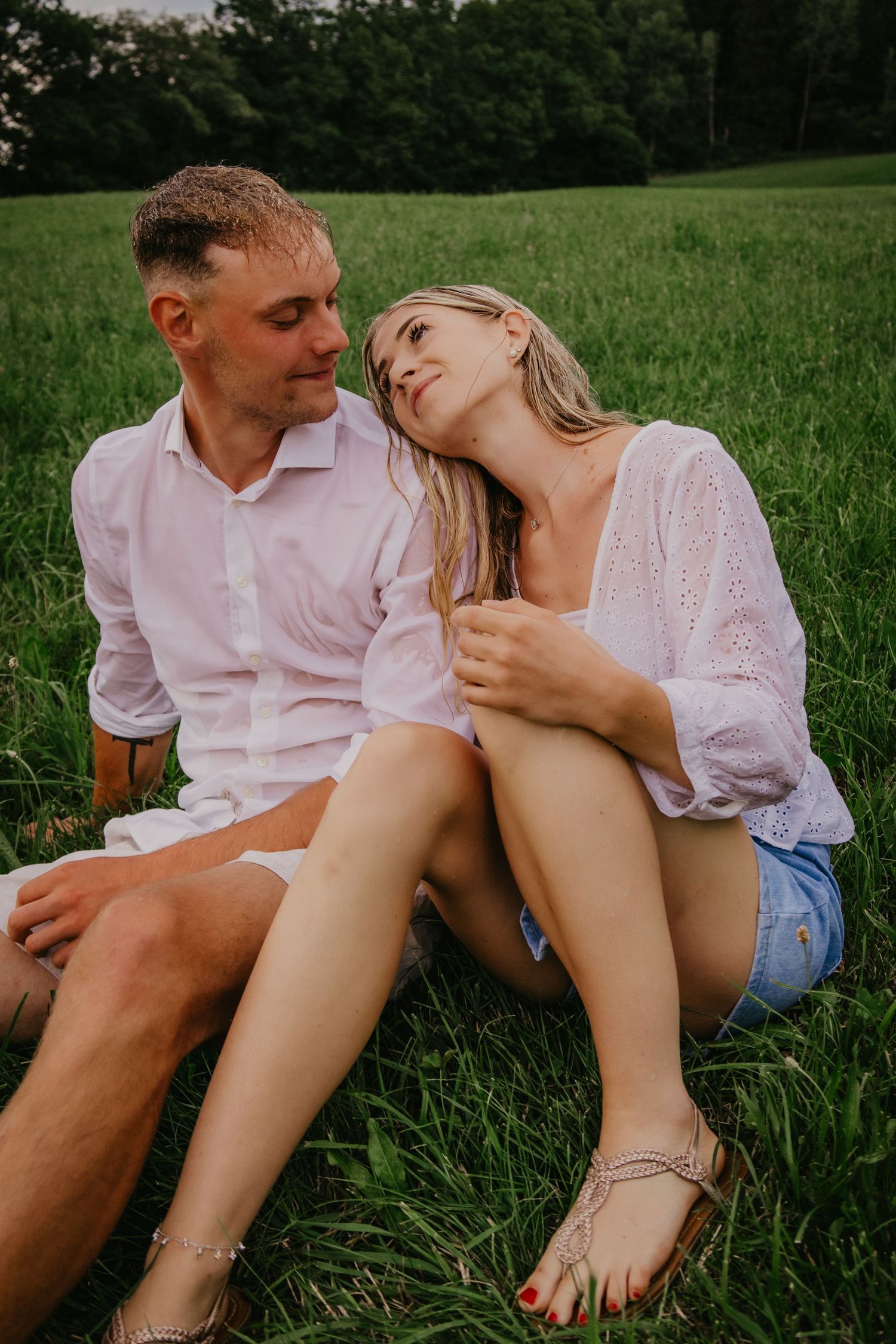 Couple sitting together on green grass, woman resting her head on mans shoulder.