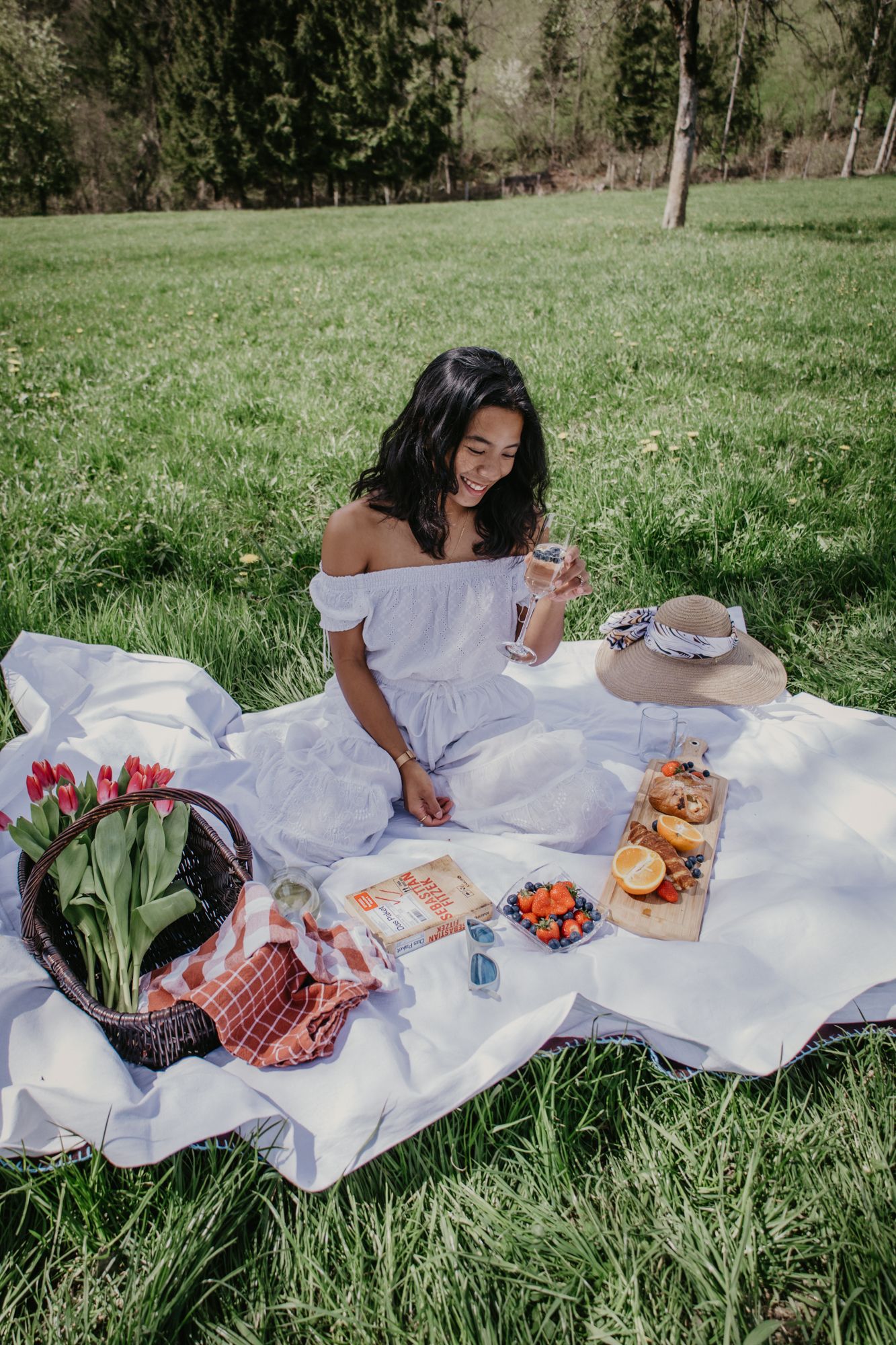 Relaxing spring picnic with fresh food and tulips laid out on white blanket.