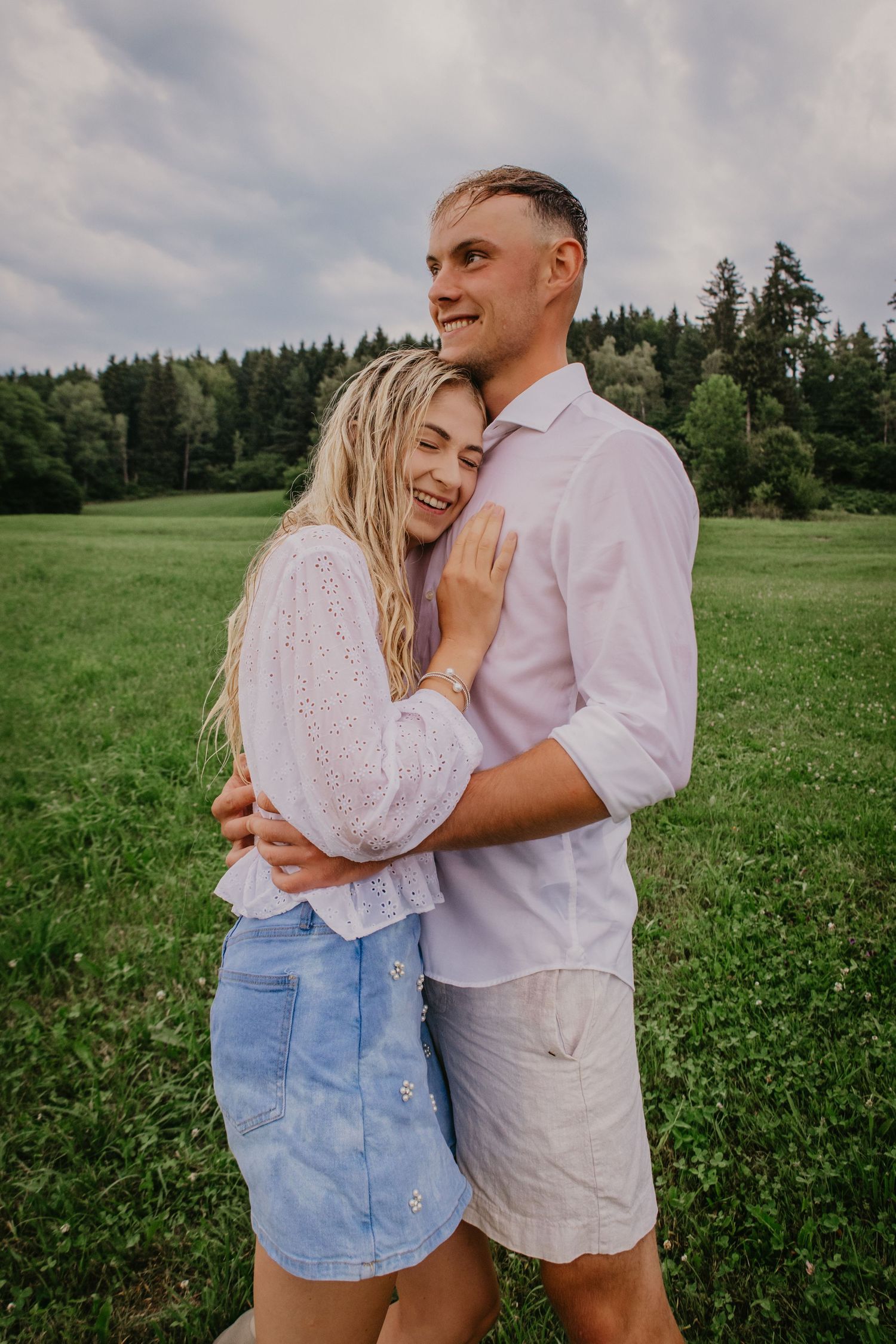 Happy couple embracing and smiling in a green field with forest background.