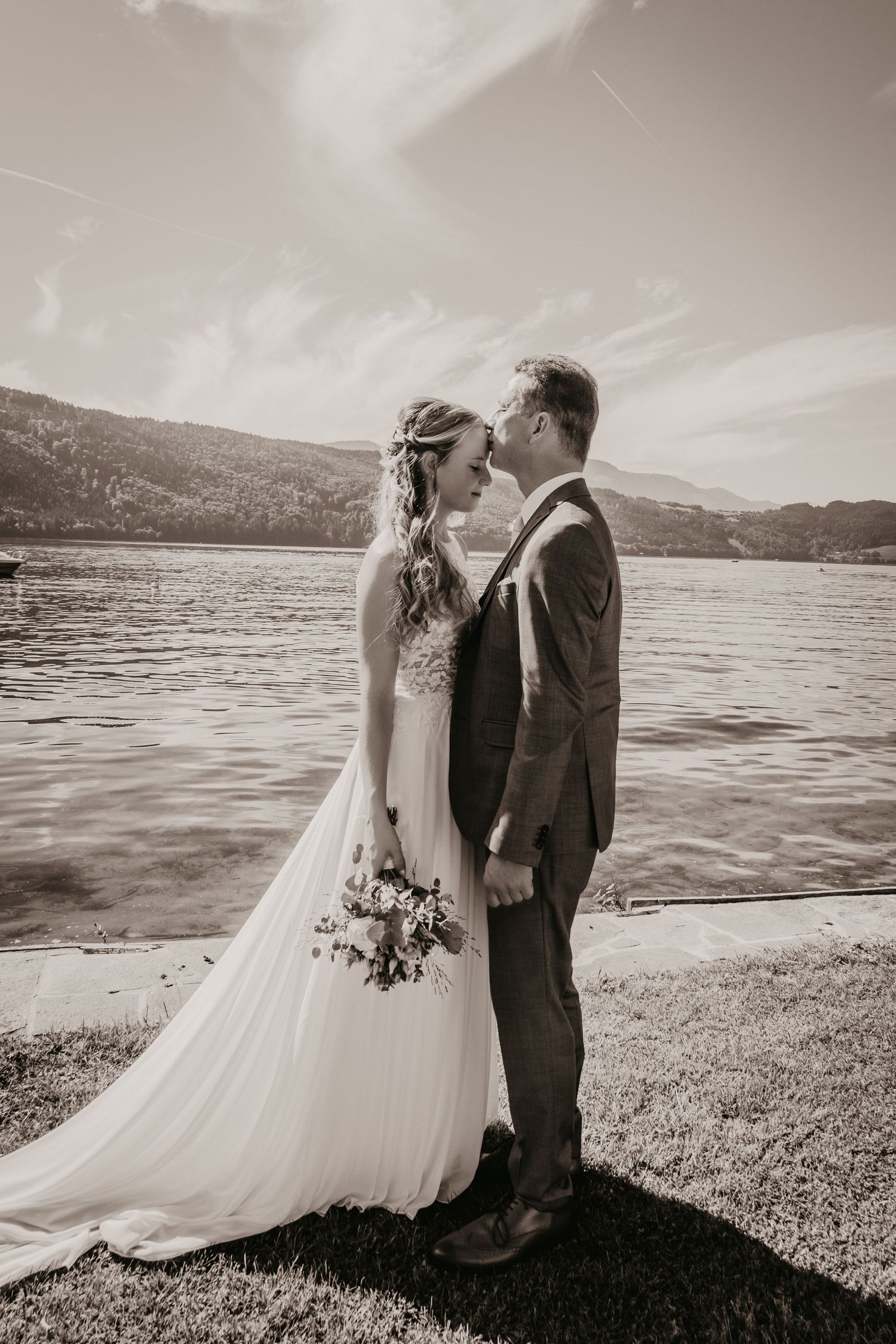 Black and white wedding portrait by a serene lake with a flowing white dress.