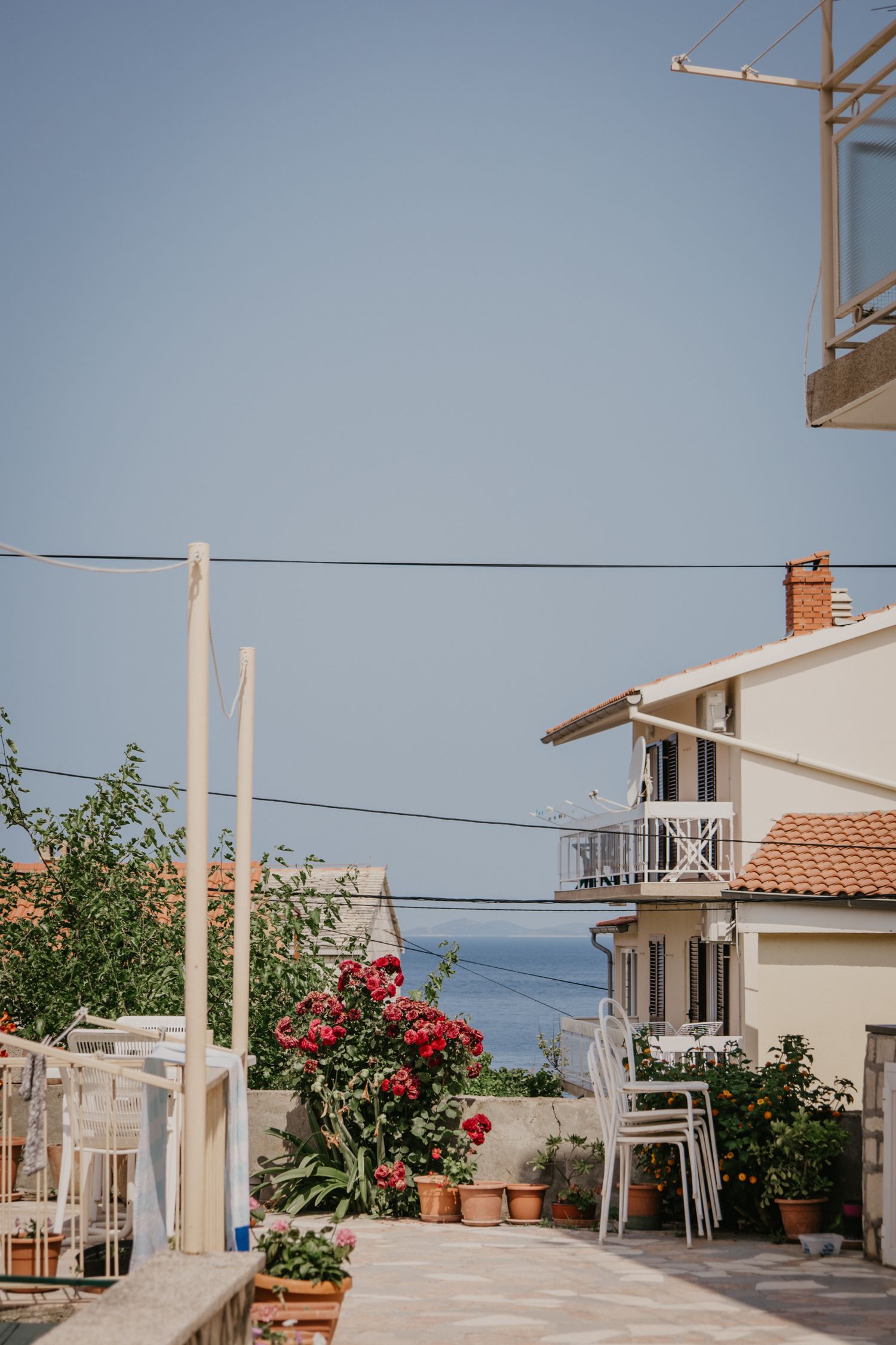 Mediterranean seaside houses with white posts and red flowers against a blue sky.