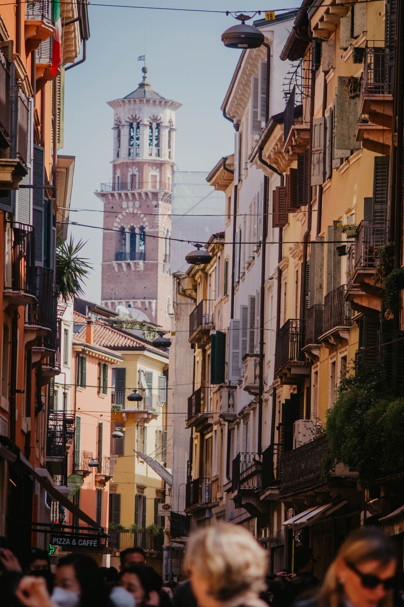 Charming Italian street with colorful buildings leading to a prominent bell tower in the distance.