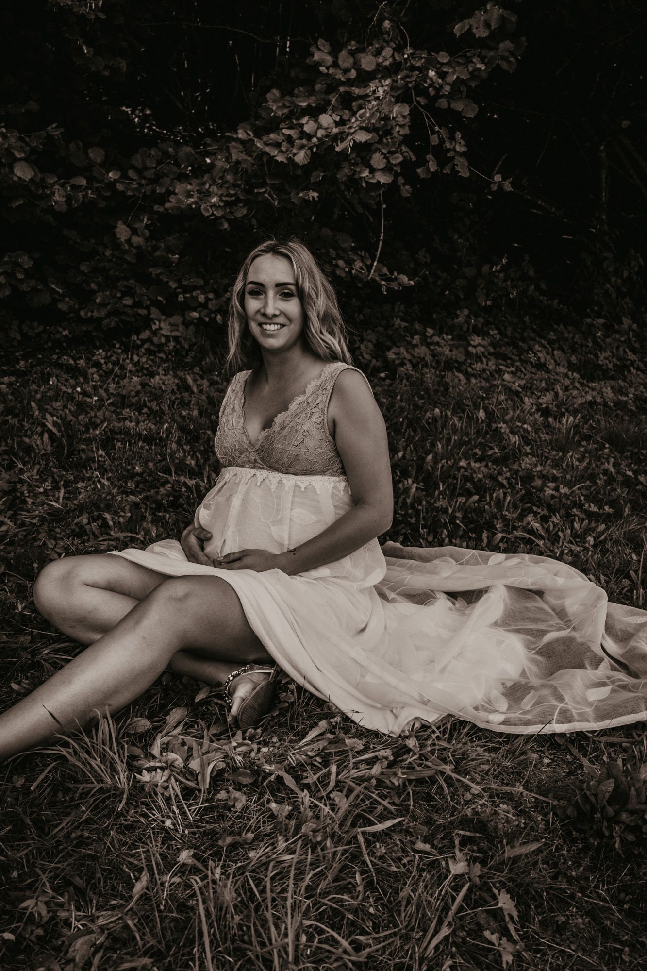A person in a white dress reclines on grass in a moody black and white photo.