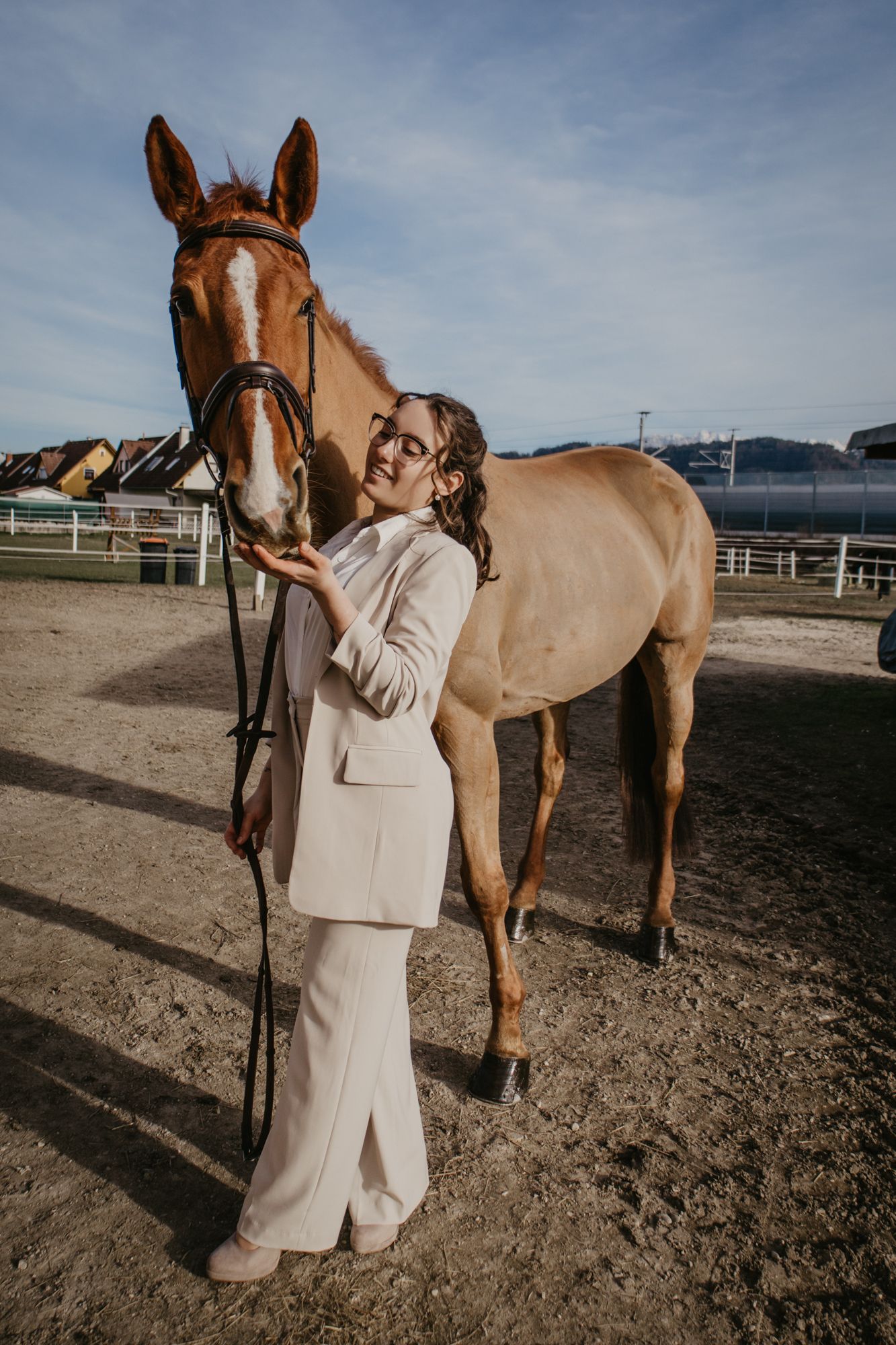 A cream-colored horse stands with someone in a light-colored suit in an outdoor arena.