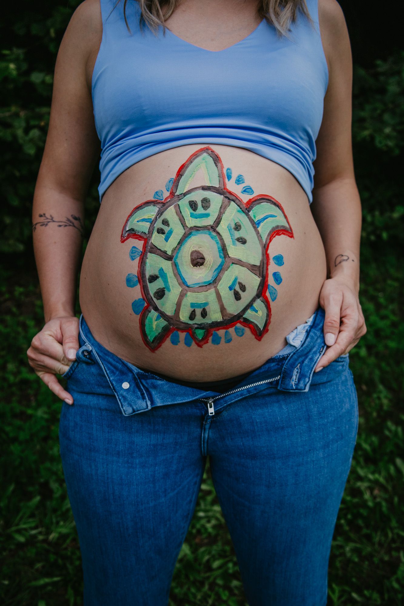 Close-up shots of a painted belly featuring a colorful circular tribal-style design in blue and green tones.