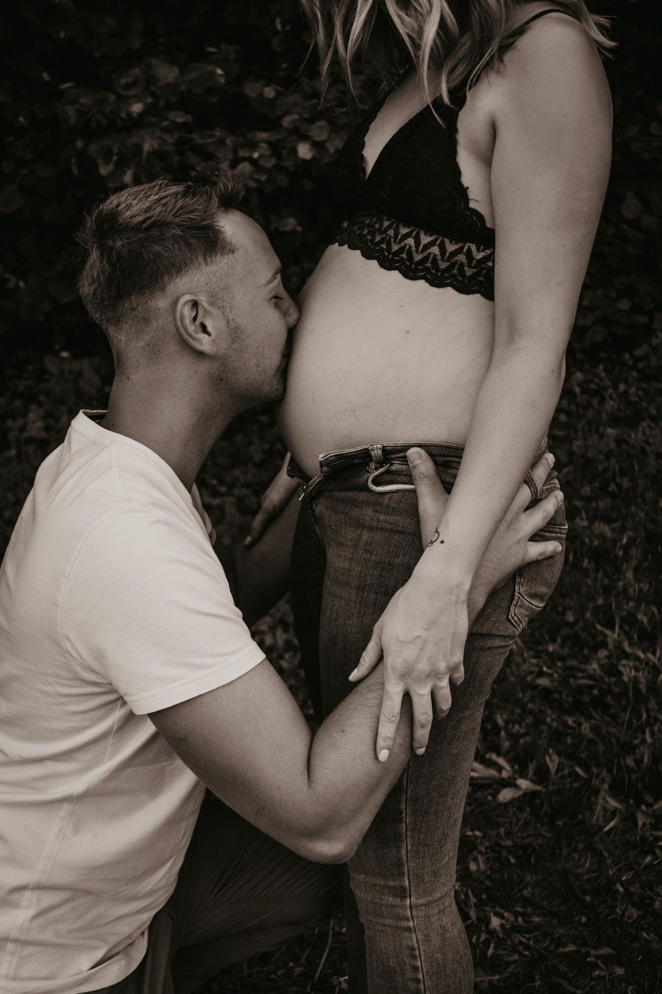 Intimate maternity photoshoot showing tender moments between couple in black and white.