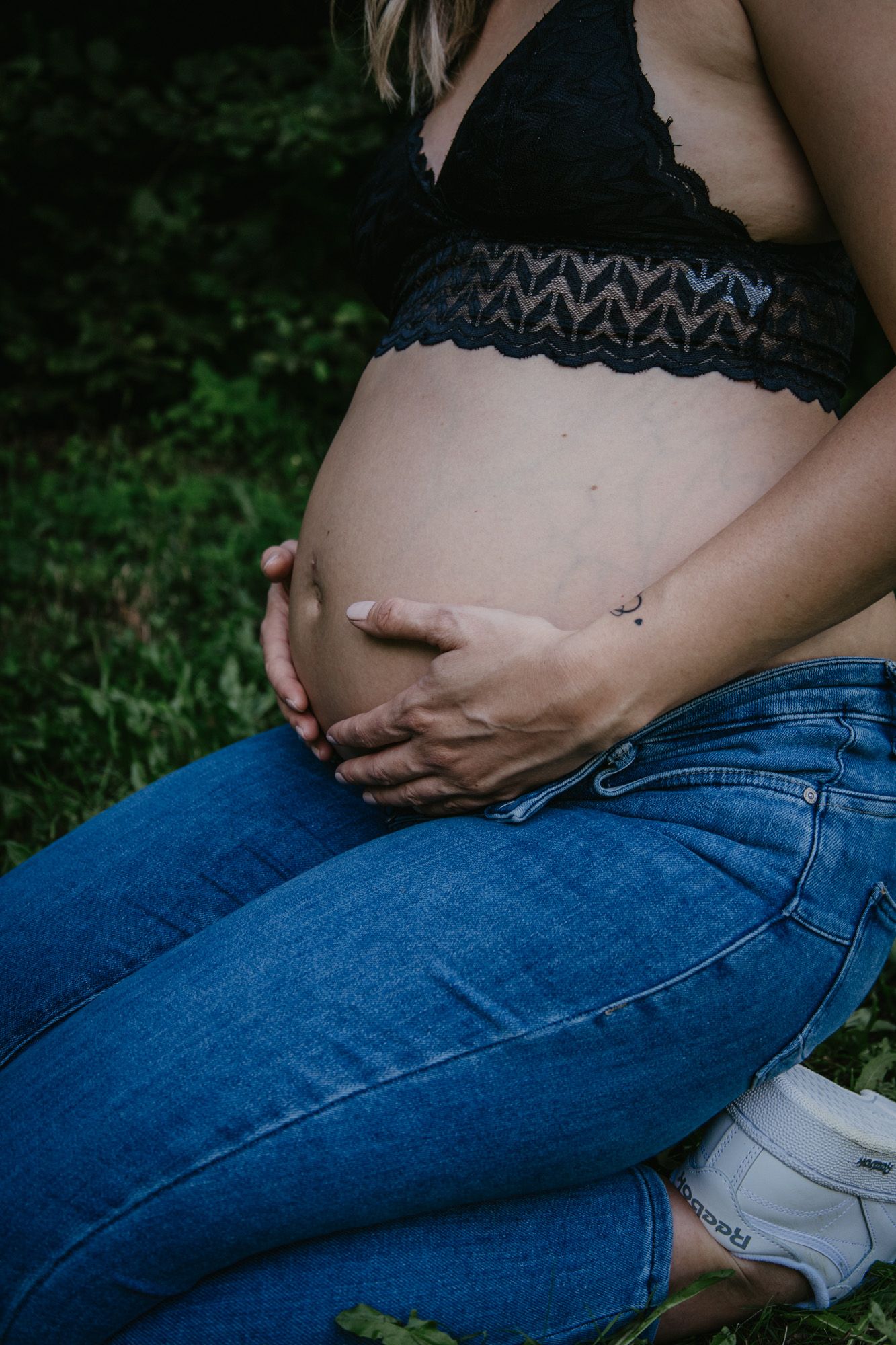 Artistic shots of pregnant belly in black lace top and jeans against dark background.
