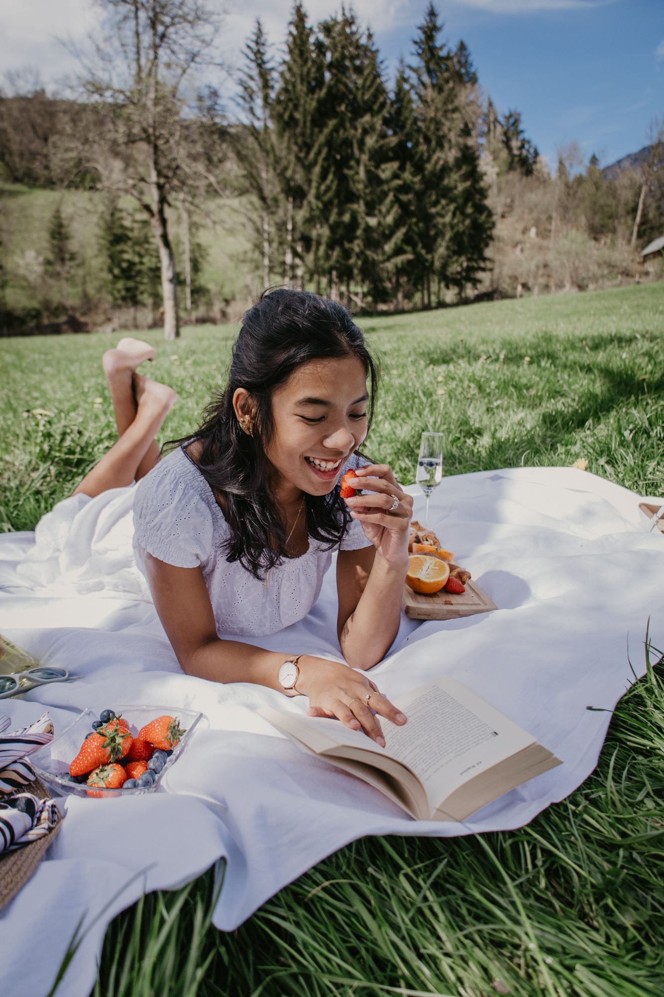 A tranquil outdoor reading scene with snacks and refreshments laid out on a white picnic blanket.