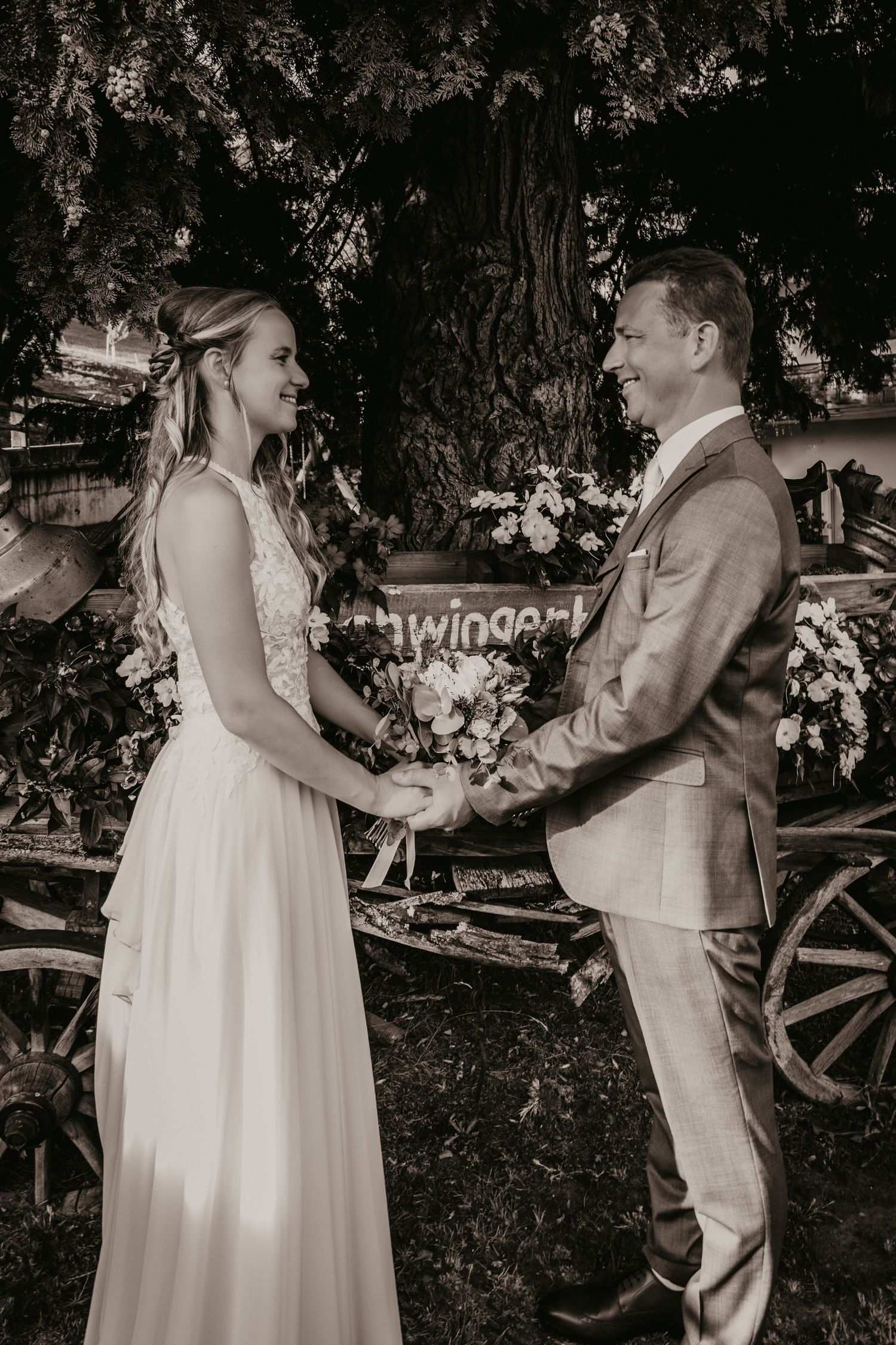 Vintage-style black and white wedding portrait with rustic wooden wagon in background.
