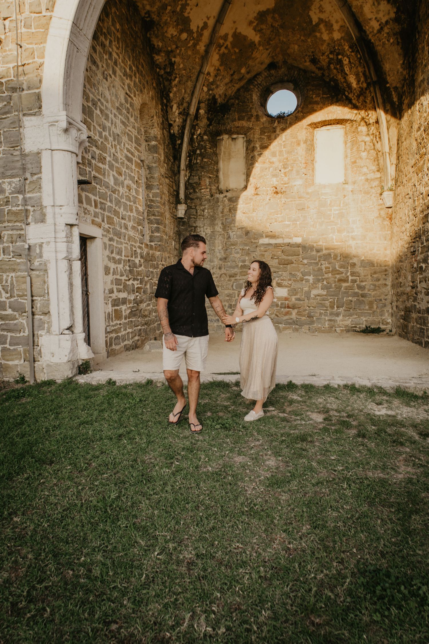 Couple enjoying playful moments under stone archways in a historic setting.