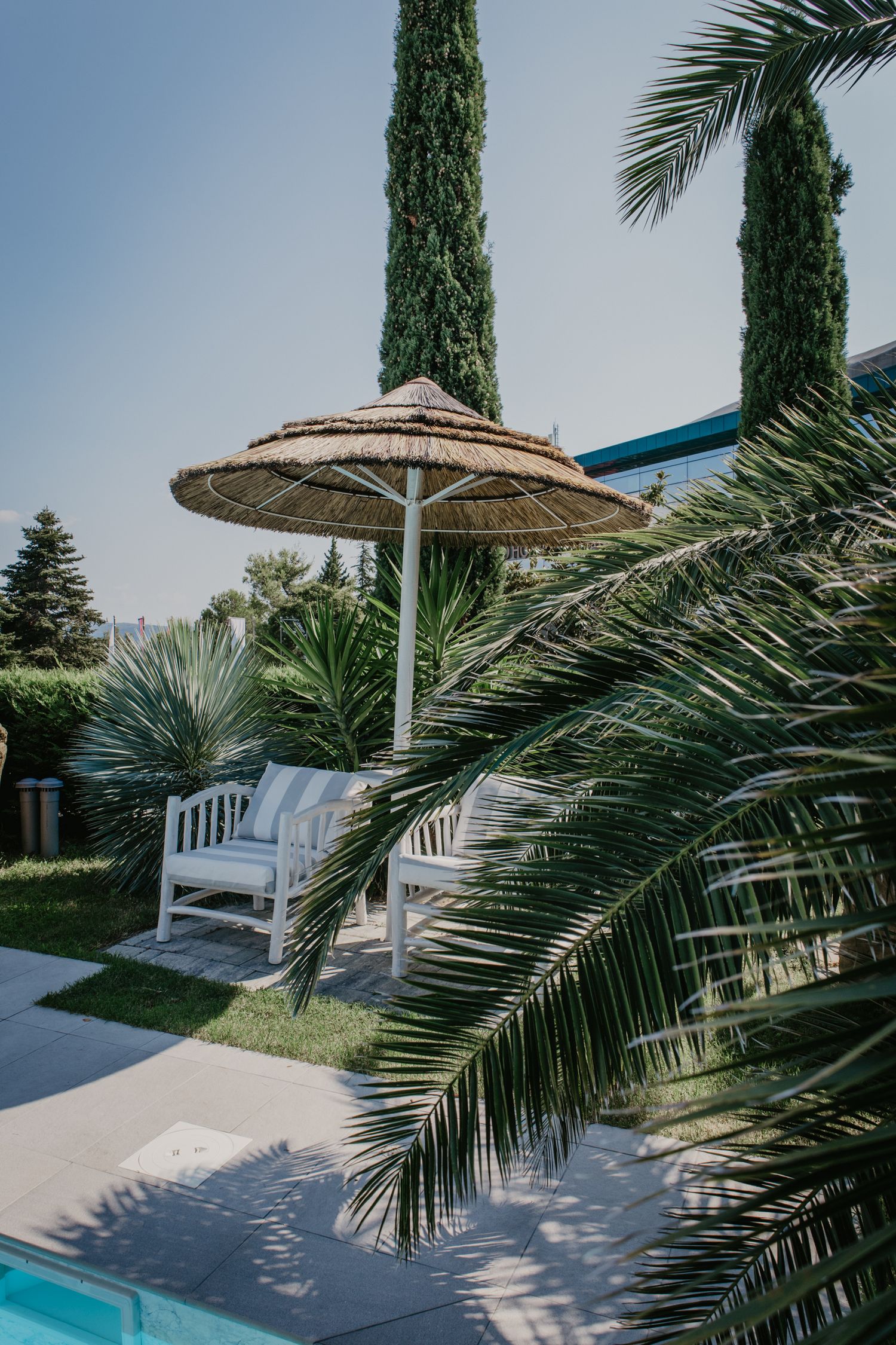 Poolside setting with palm trees and thatched umbrellas creating a tropical resort atmosphere.