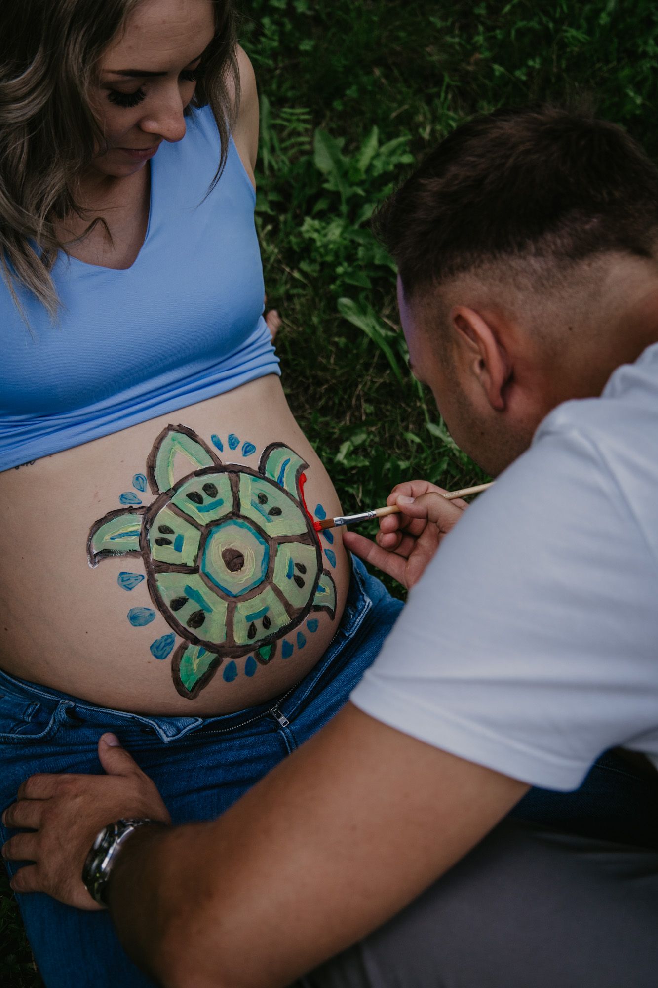 Colorful belly painting session showing creation of decorative mandala design.