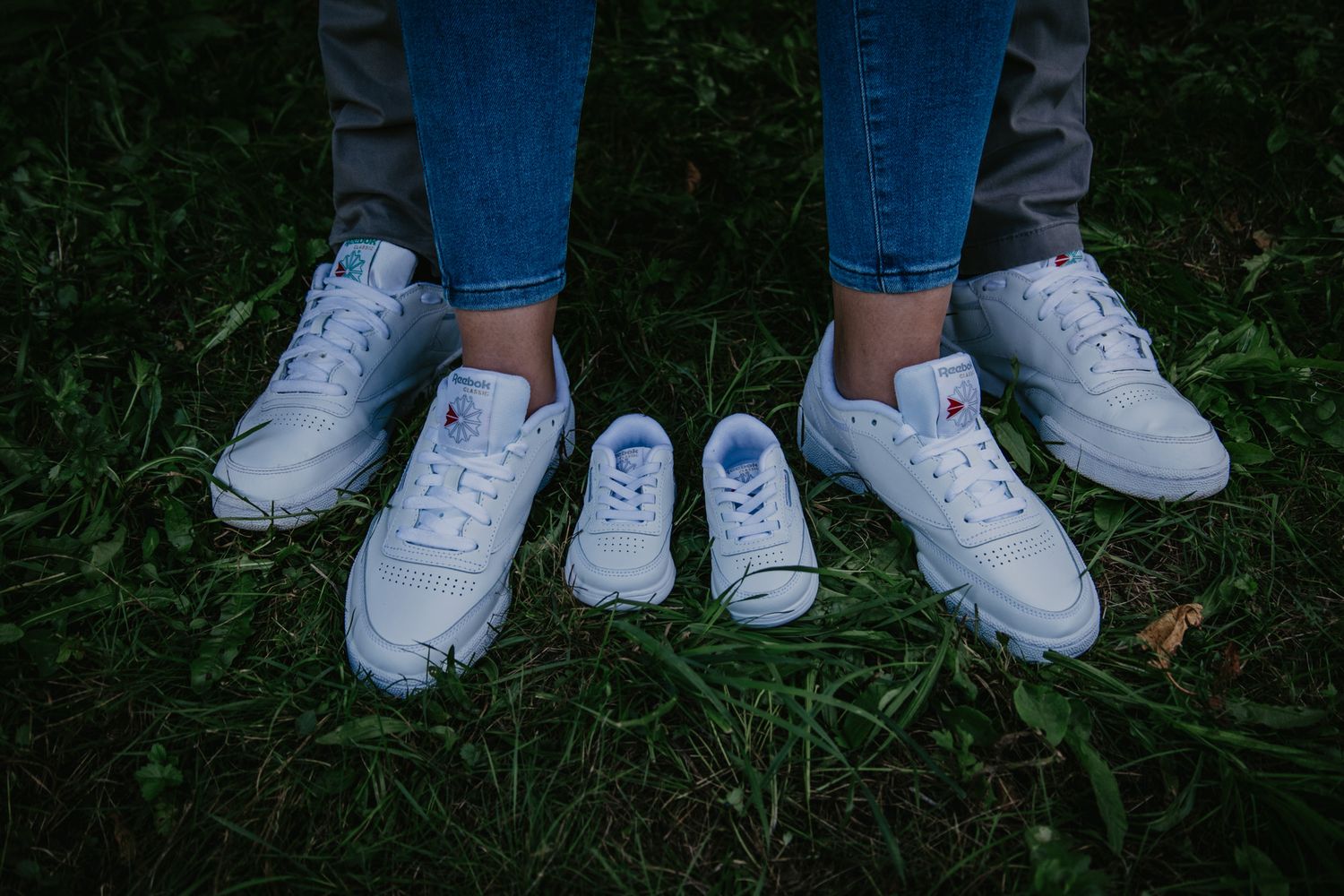 Row of white sneakers on grass showing matching footwear.