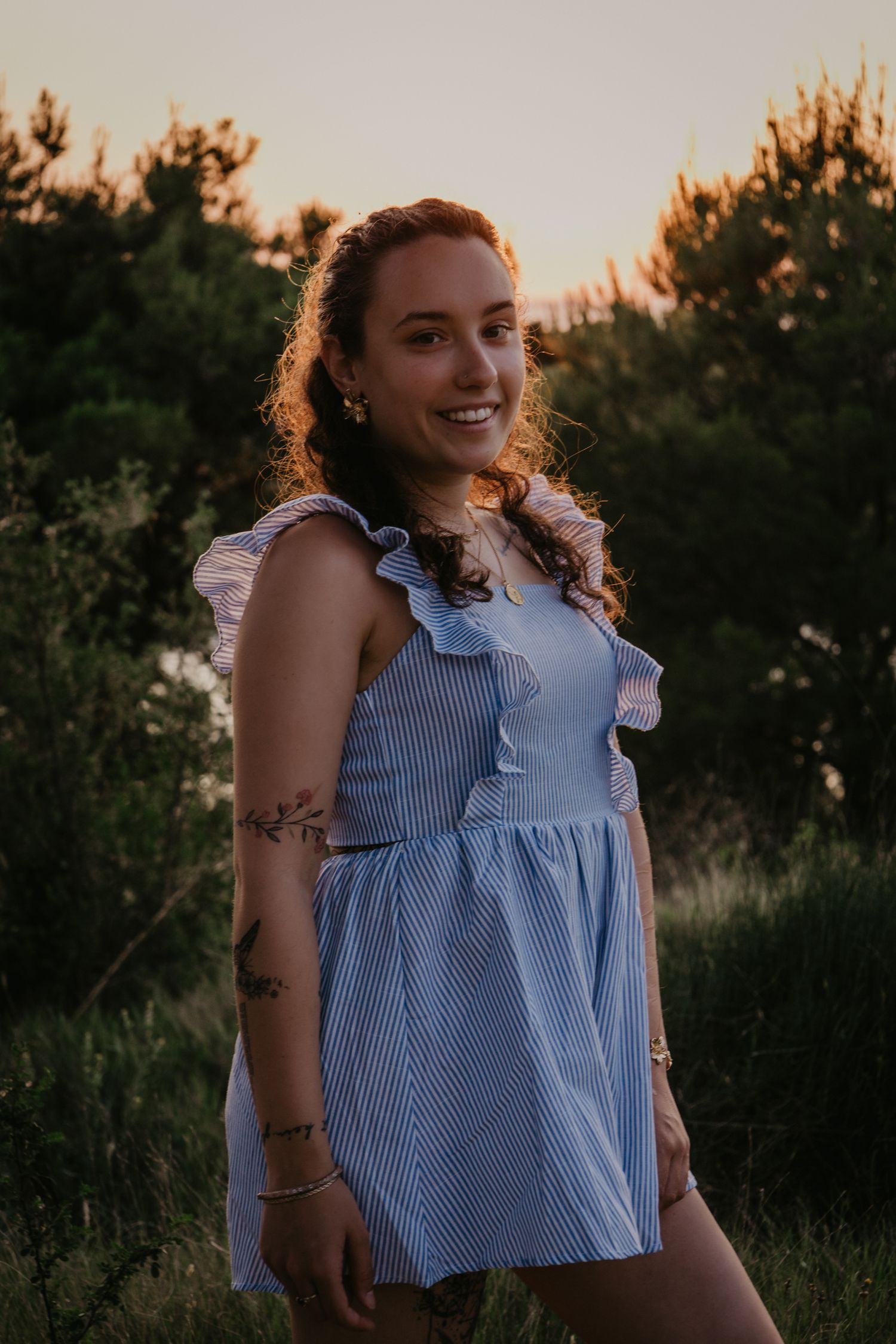 Portrait against golden sunset light wearing a blue and white striped sleeveless top with ruffles.