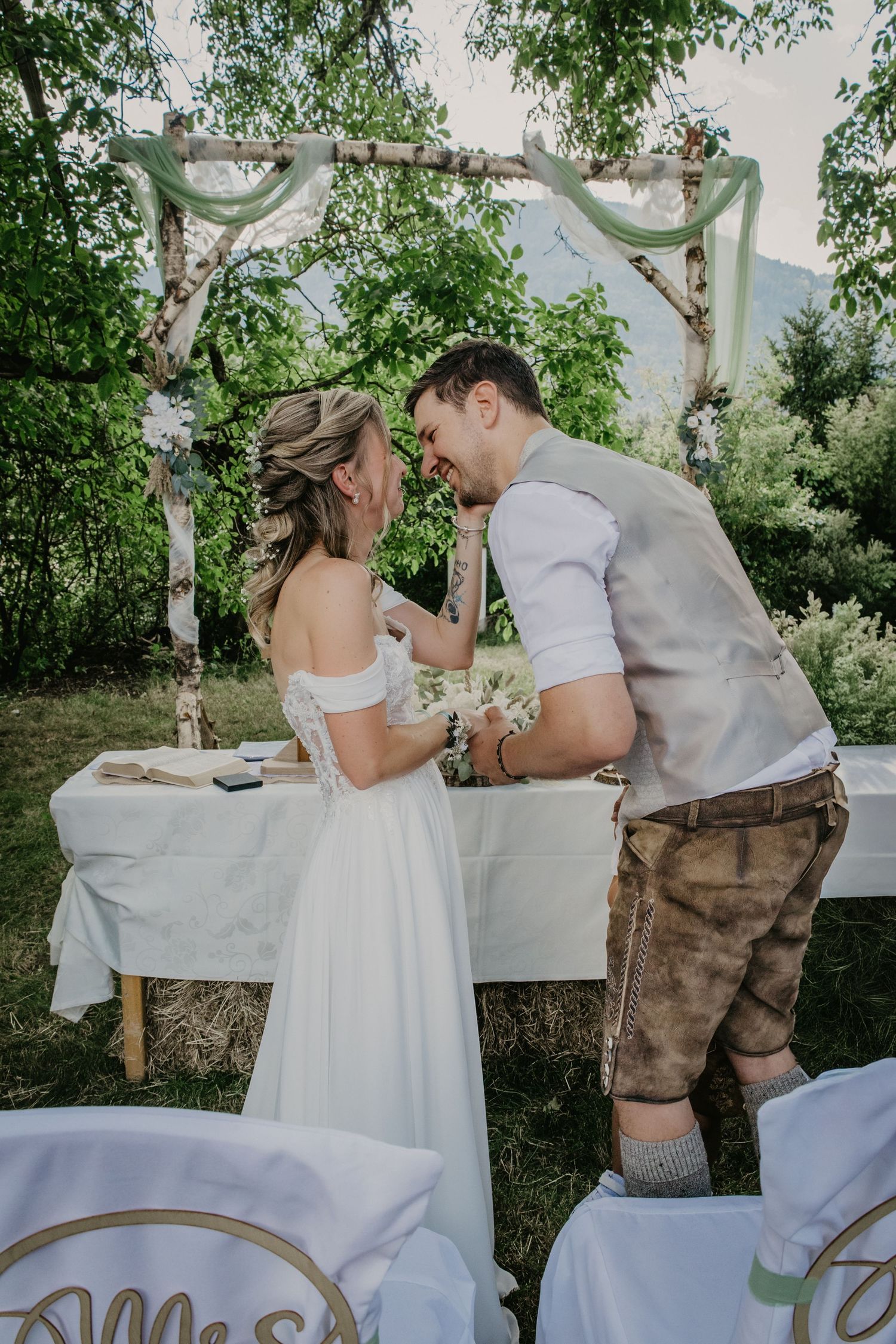 Bride and groom sharing an intimate moment at outdoor rustic birch wedding arch ceremony in a green garden setting.