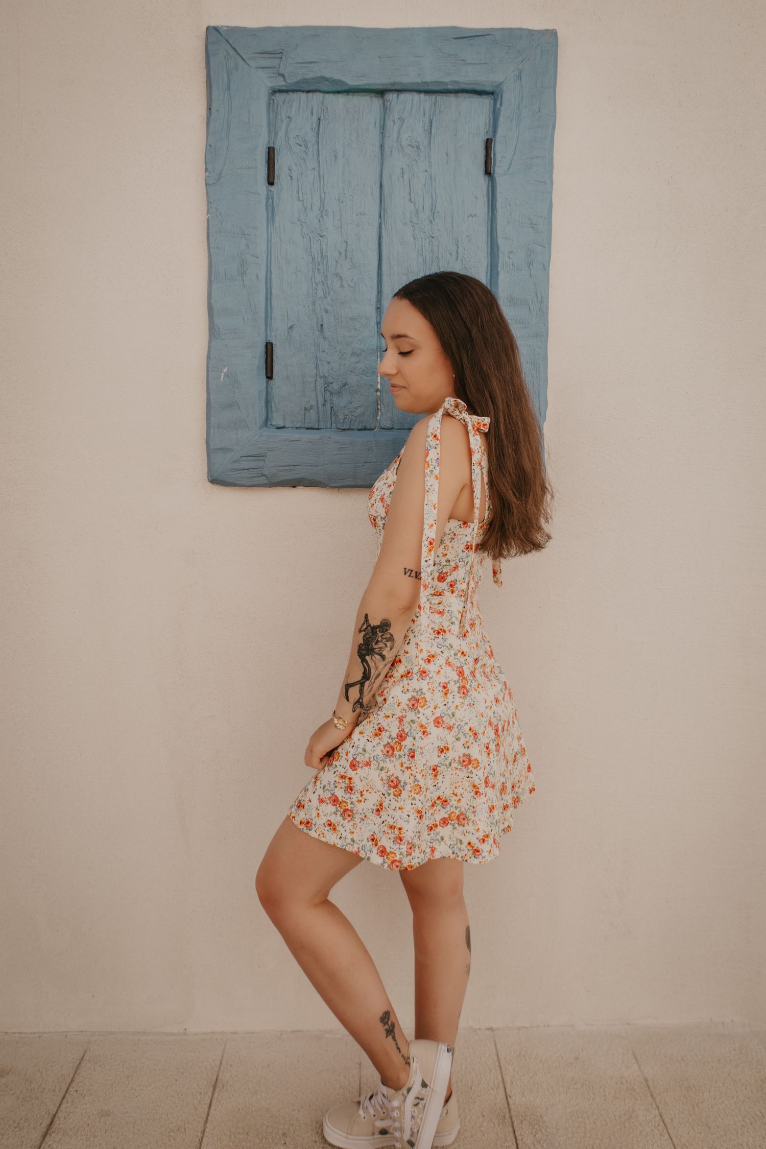 Playful poses in a floral dress against rustic blue shutters and white wall.