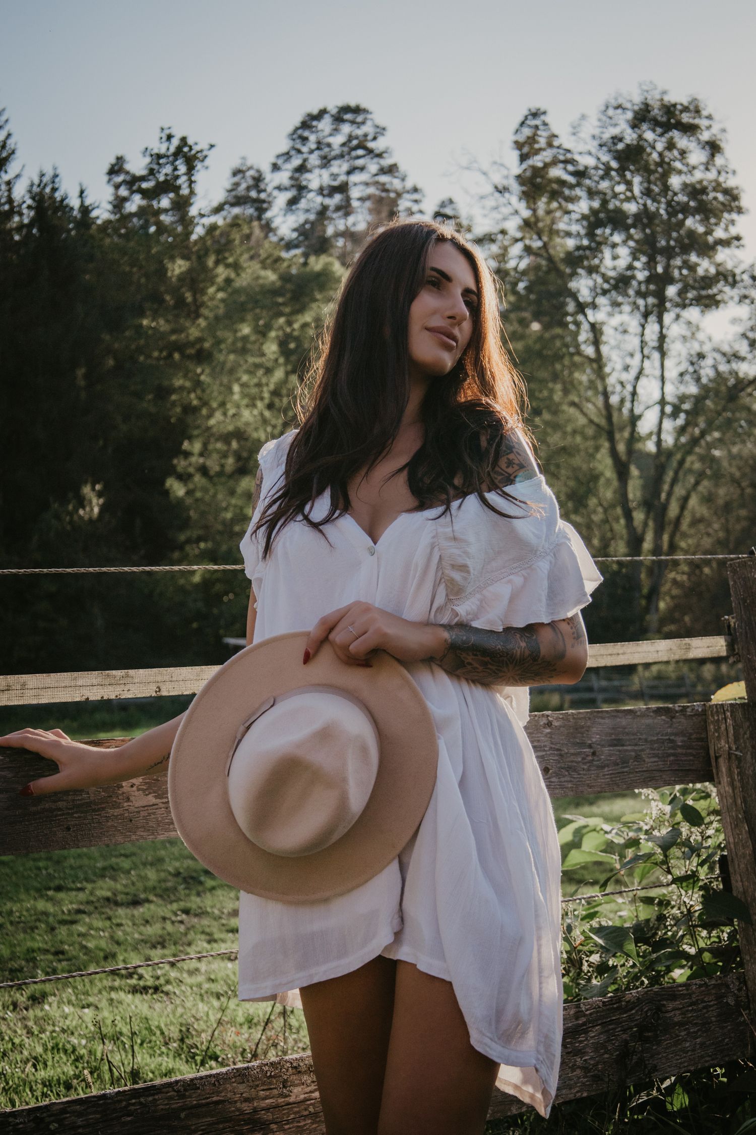Natural light portrait with white dress and hat in rustic farm setting.
