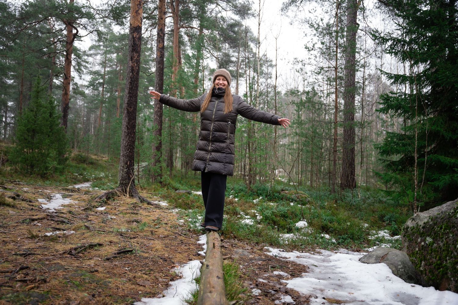 A person walks along a snowy forest trail surrounded by tall pine trees in winter.