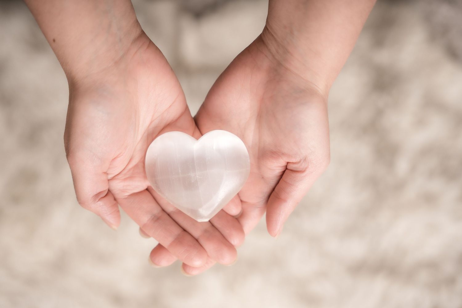 Two hands gently hold a white heart-shaped object against a soft blurred background.