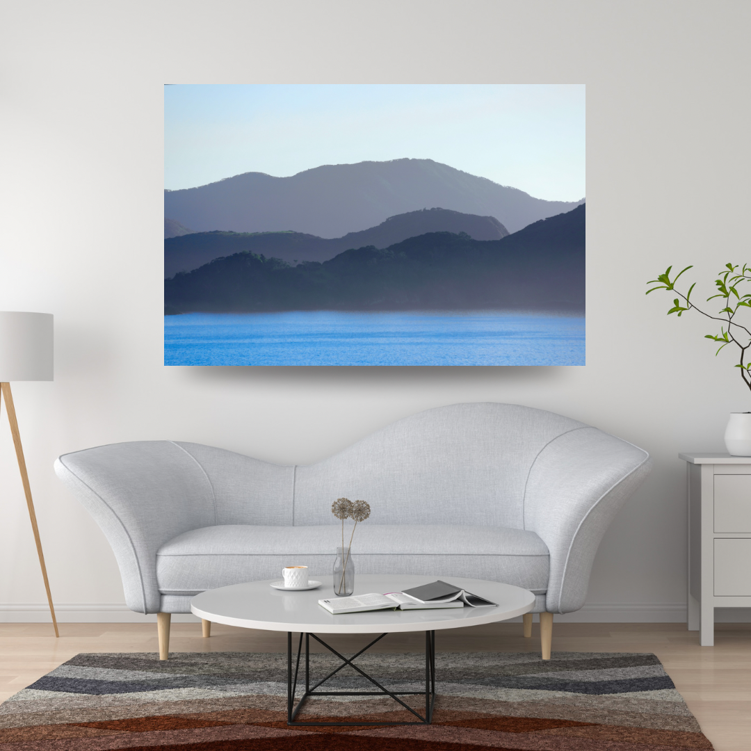 Blue mountain landscape canvas wall art displayed above a white sofa in a modern living room interior.