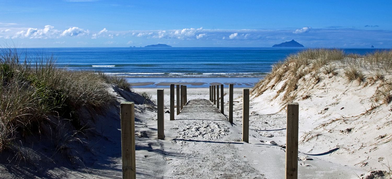 Beachfront boardwalk with wooden posts leading to ocean views and distant mountains.