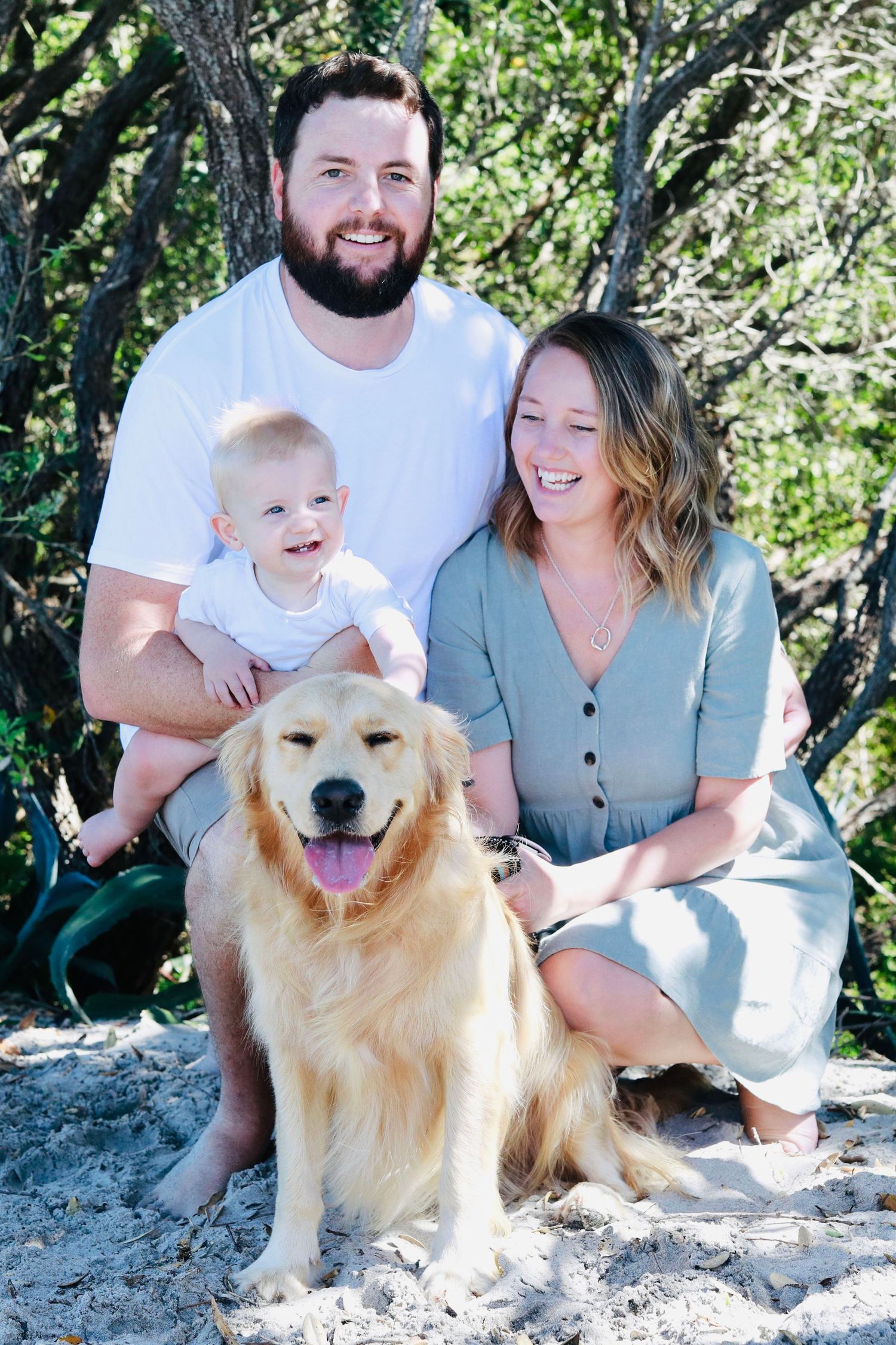 Golden Retriever and family pose together on rocky terrain with lush greenery behind them.