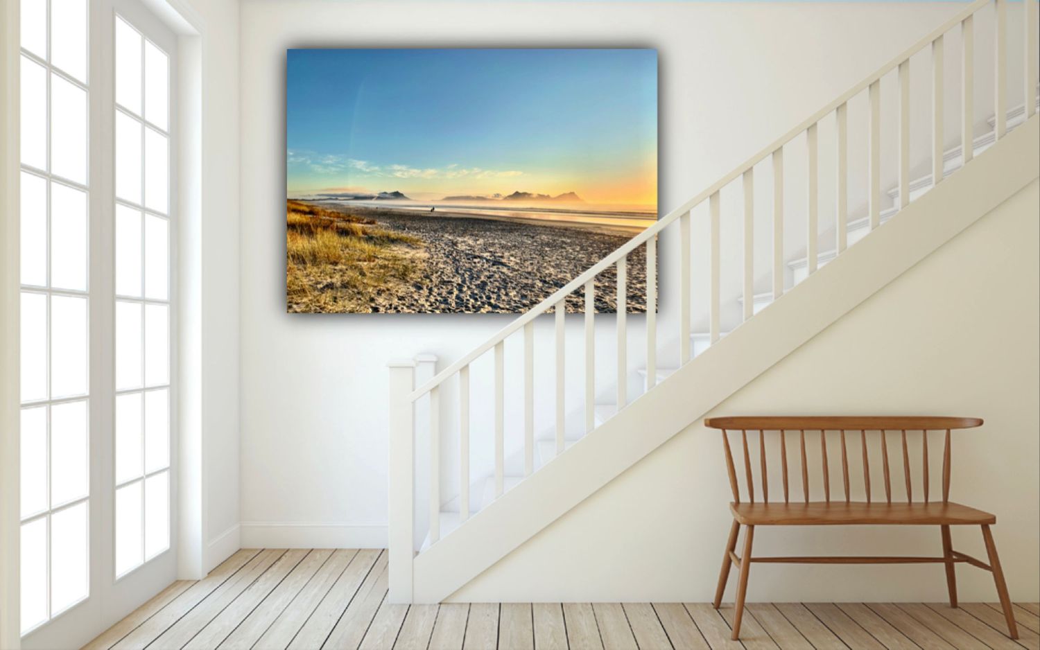 Canvas wall art of a serene beach sunset with rocky shore displayed in a bright modern hallway near stairs.