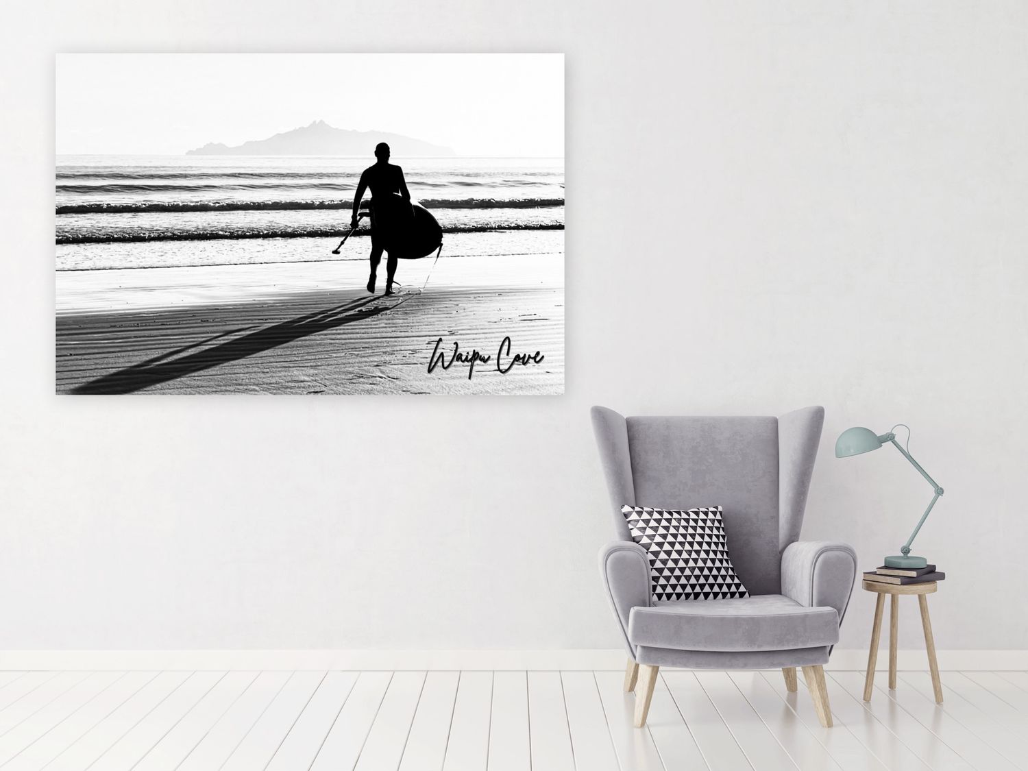 Black and white photo print of a surfer silhouette on beach displayed on wall above gray armchair in modern living room.