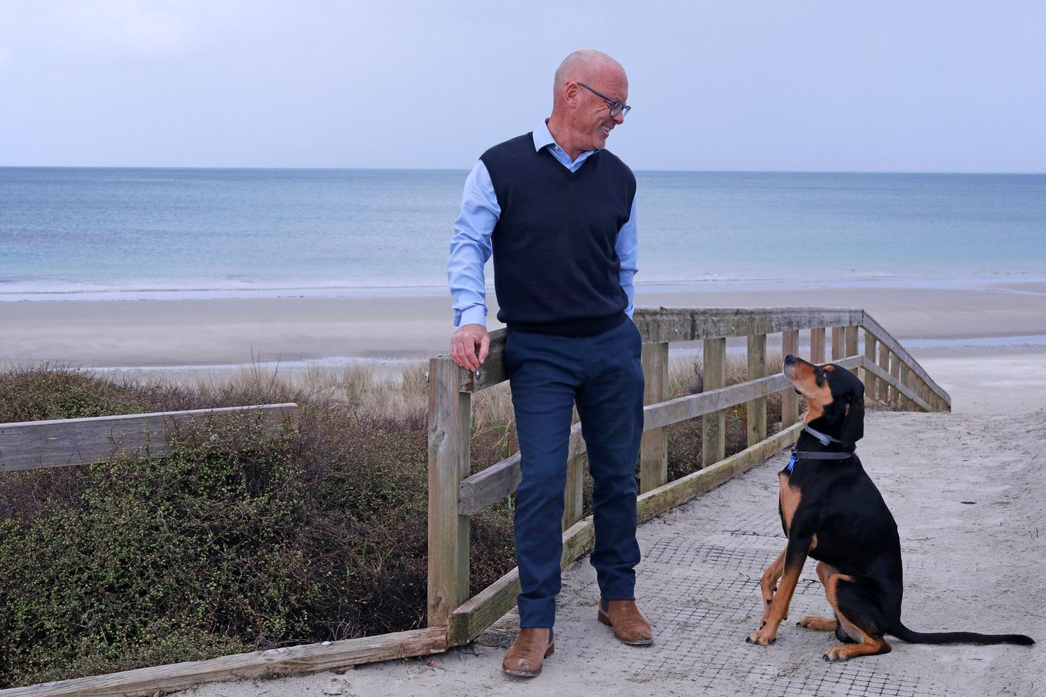 Standing on beach boardwalk with black dog against ocean backdrop.