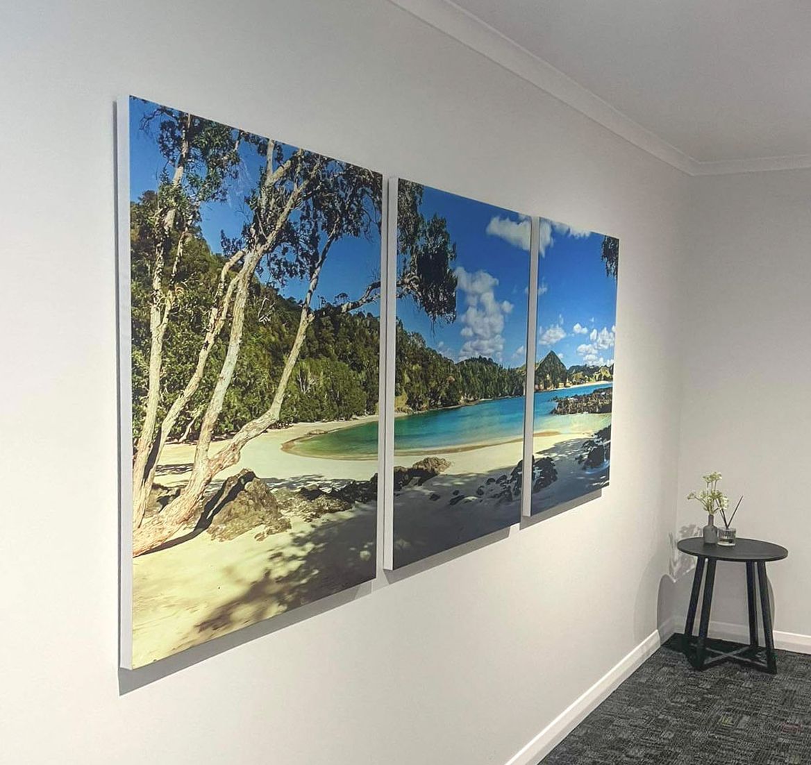 Triptych canvas wall art of a tropical beach with turquoise water, white sand, and lush green trees displayed in a modern room.