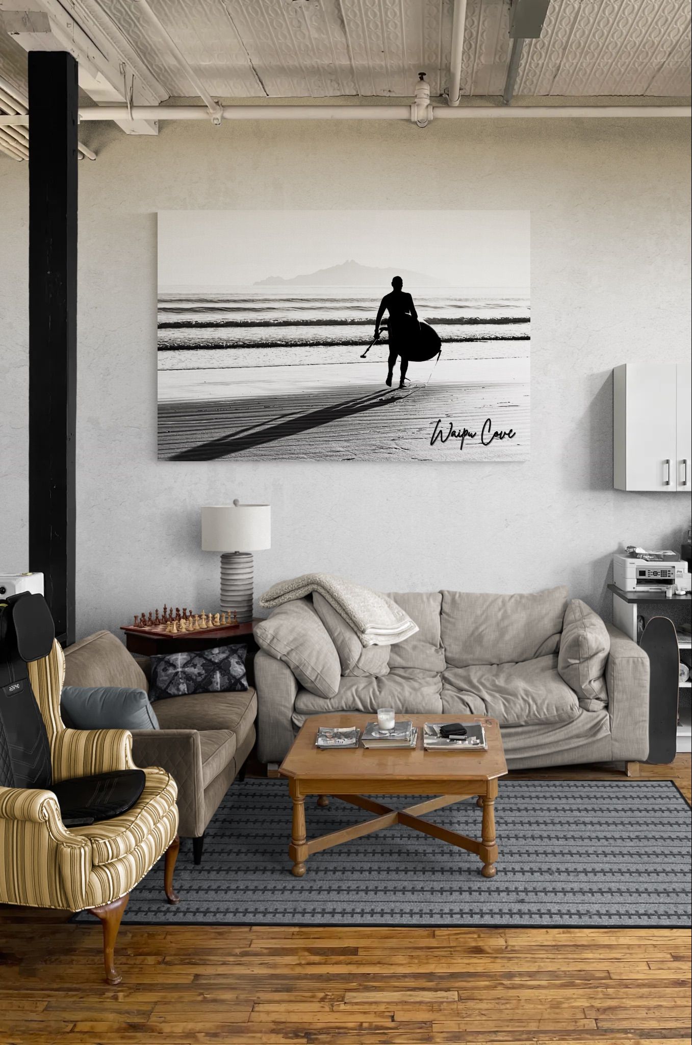 Black and white surfer wall art above a gray sofa in a modern living room with hardwood floors and industrial ceiling.