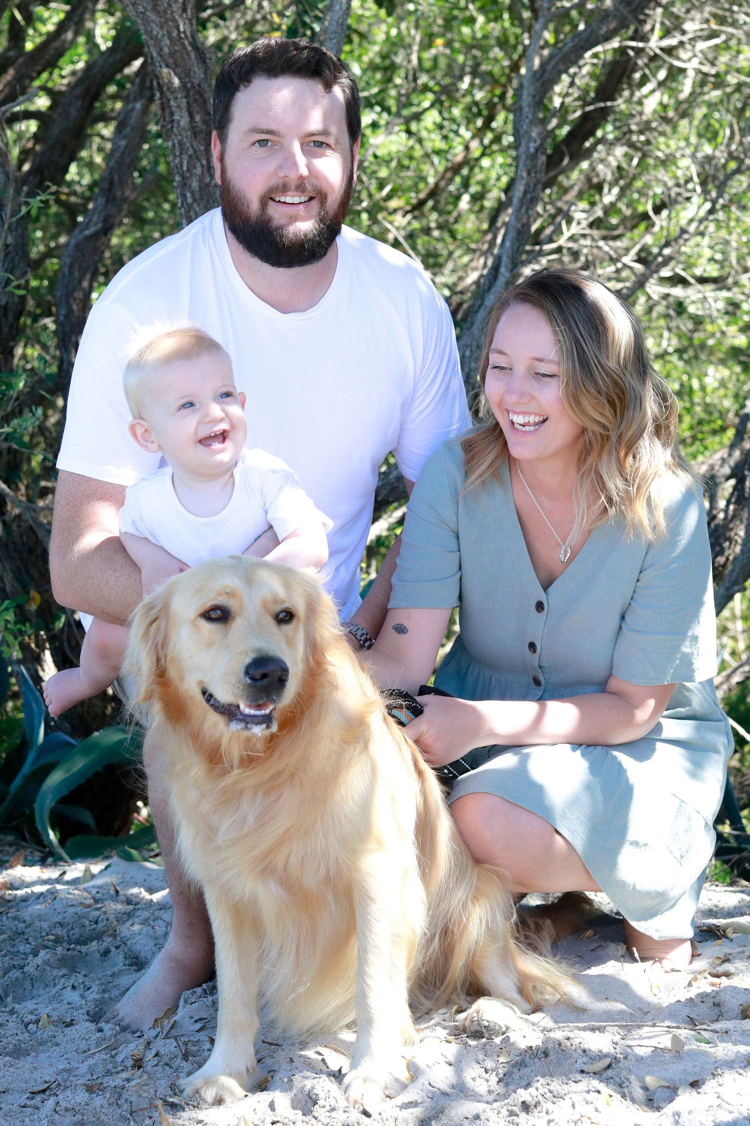 Golden Retriever smiles during family photo session on rocky terrain with trees.