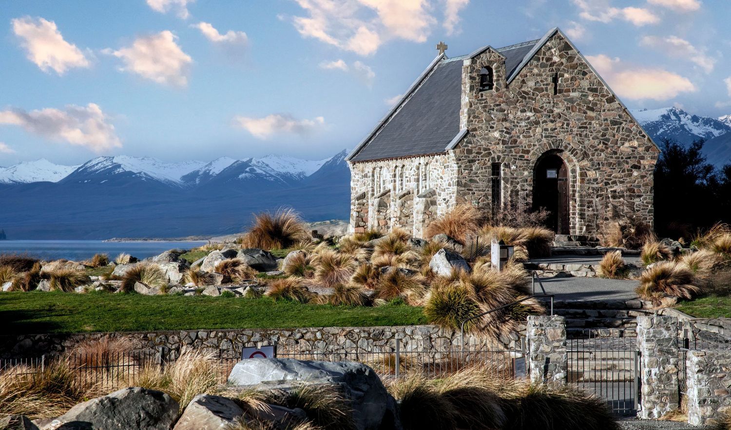 Stone church by alpine lake with snow-capped mountains backdrop, Church of the Good Shepherd, Lake Tekapo, New Zealand.