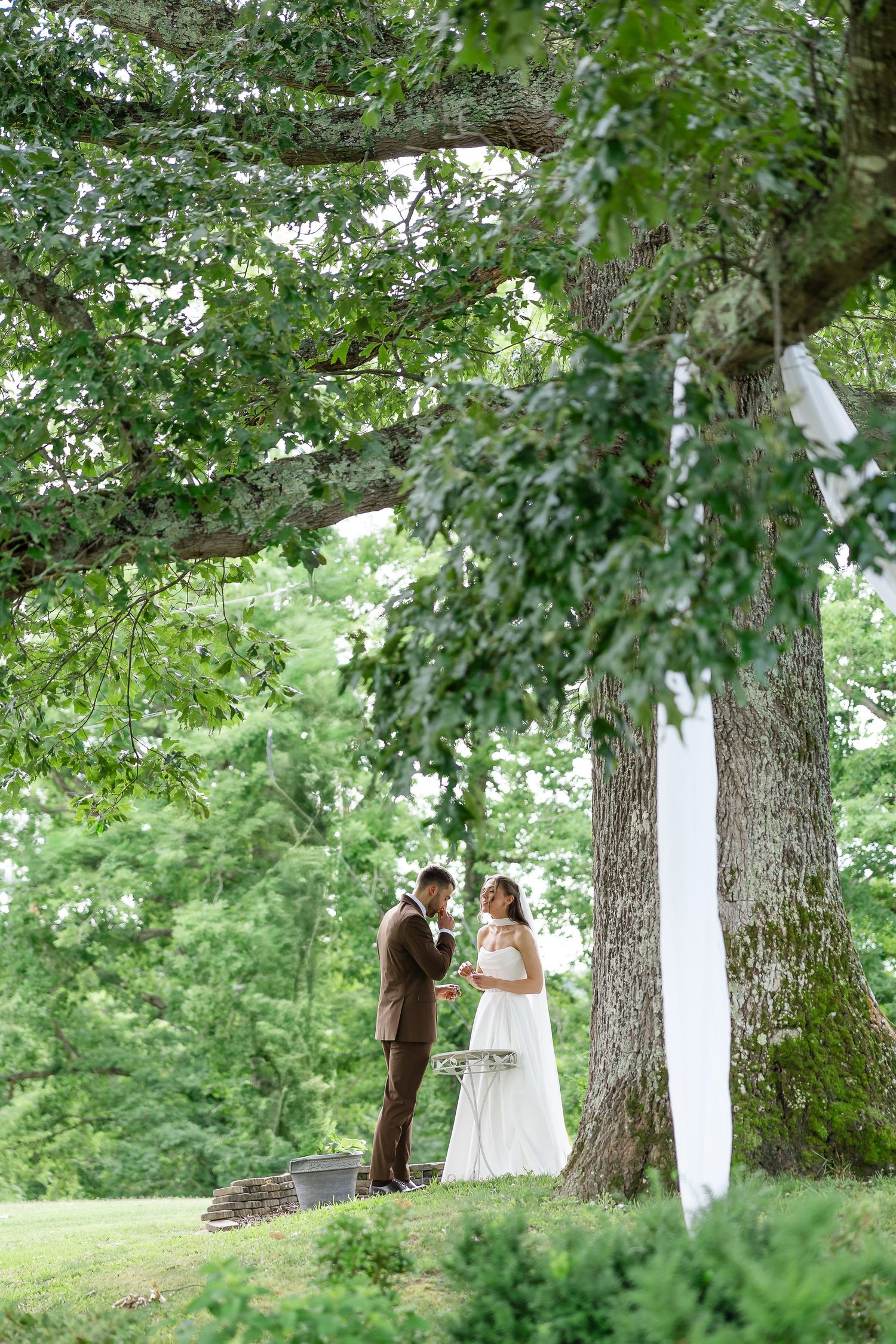 Bride and groom stand together under a large oak tree in a lush green outdoor wedding setting at front porch farms, in Charlotte tennessee