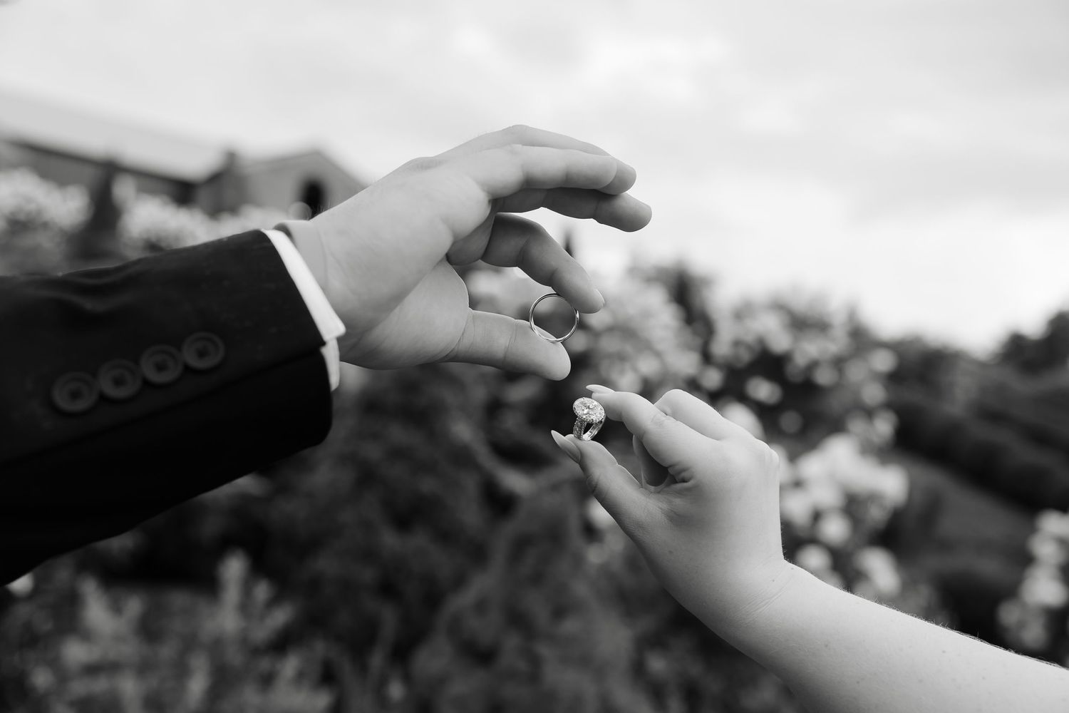 Black and white photo of a groom placing a wedding ring on the bride's finger during a ceremony.