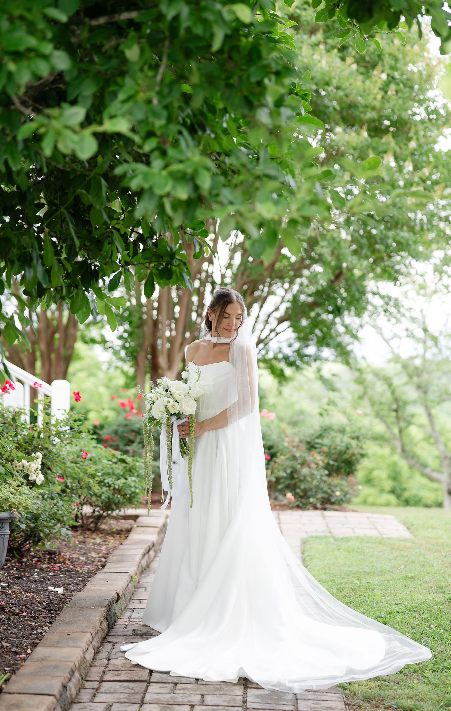 Bride in white gown and veil holds bouquet in lush garden setting.at front porch farms, in Charlotte tennessee