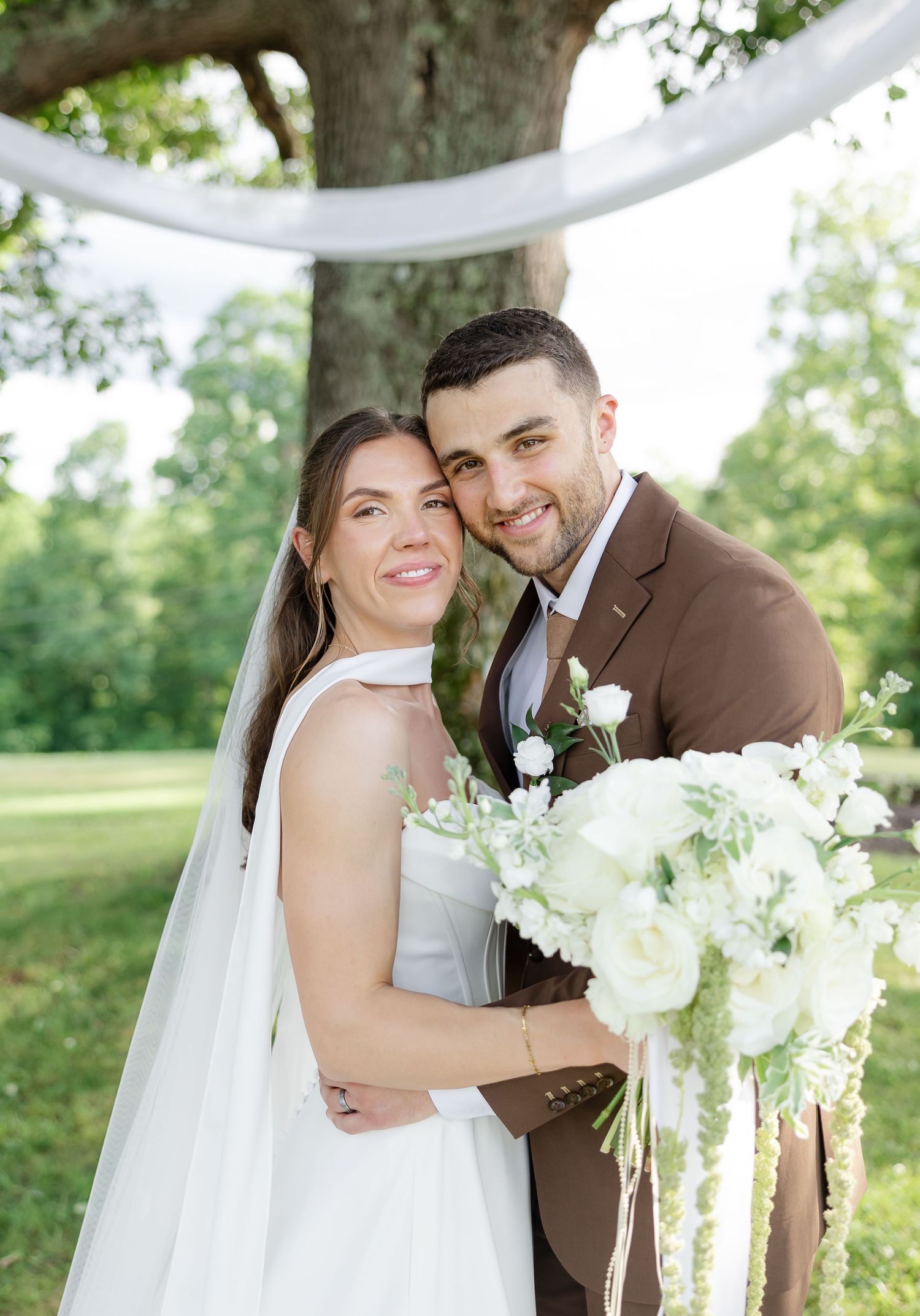 Bride and groom smiling together outdoors under a floral arch,  at front porch farms in Charlotte TN