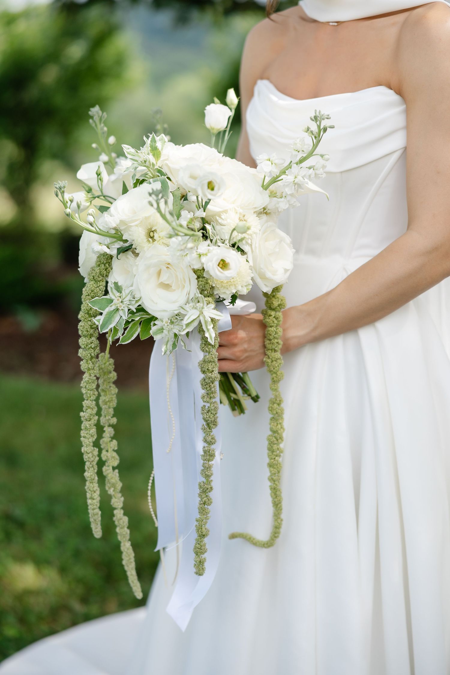 Bride in white strapless gown holding elegant bouquet of white ranunculus and cascading green amaranthus with ribbon.