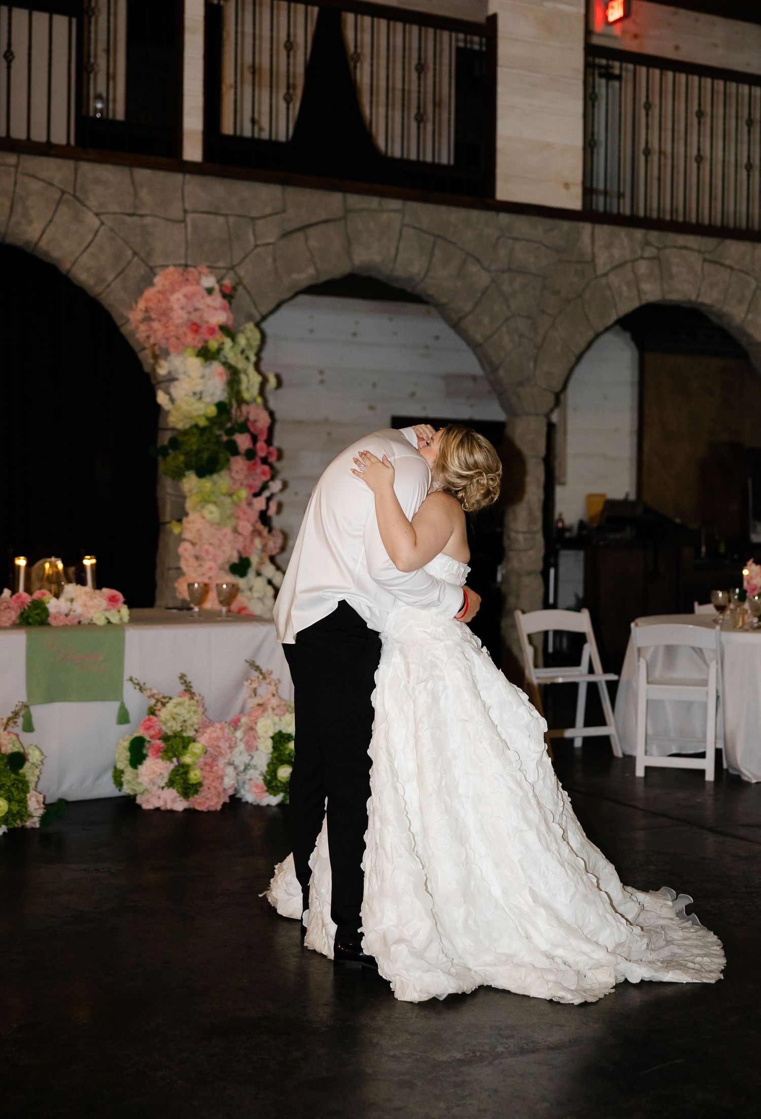 Bride and groom share first dance in elegant stone venue adorned with pink floral arrangements and candlelit tables.