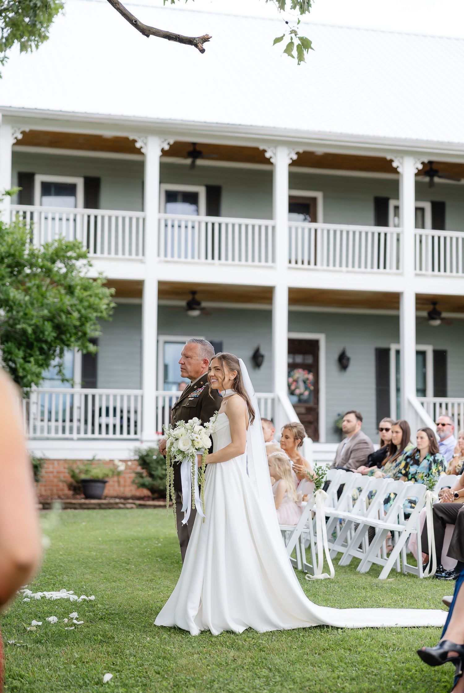 Bride and groom walk down outdoor aisle at elegant Southern estate wedding ceremony with white chairs.