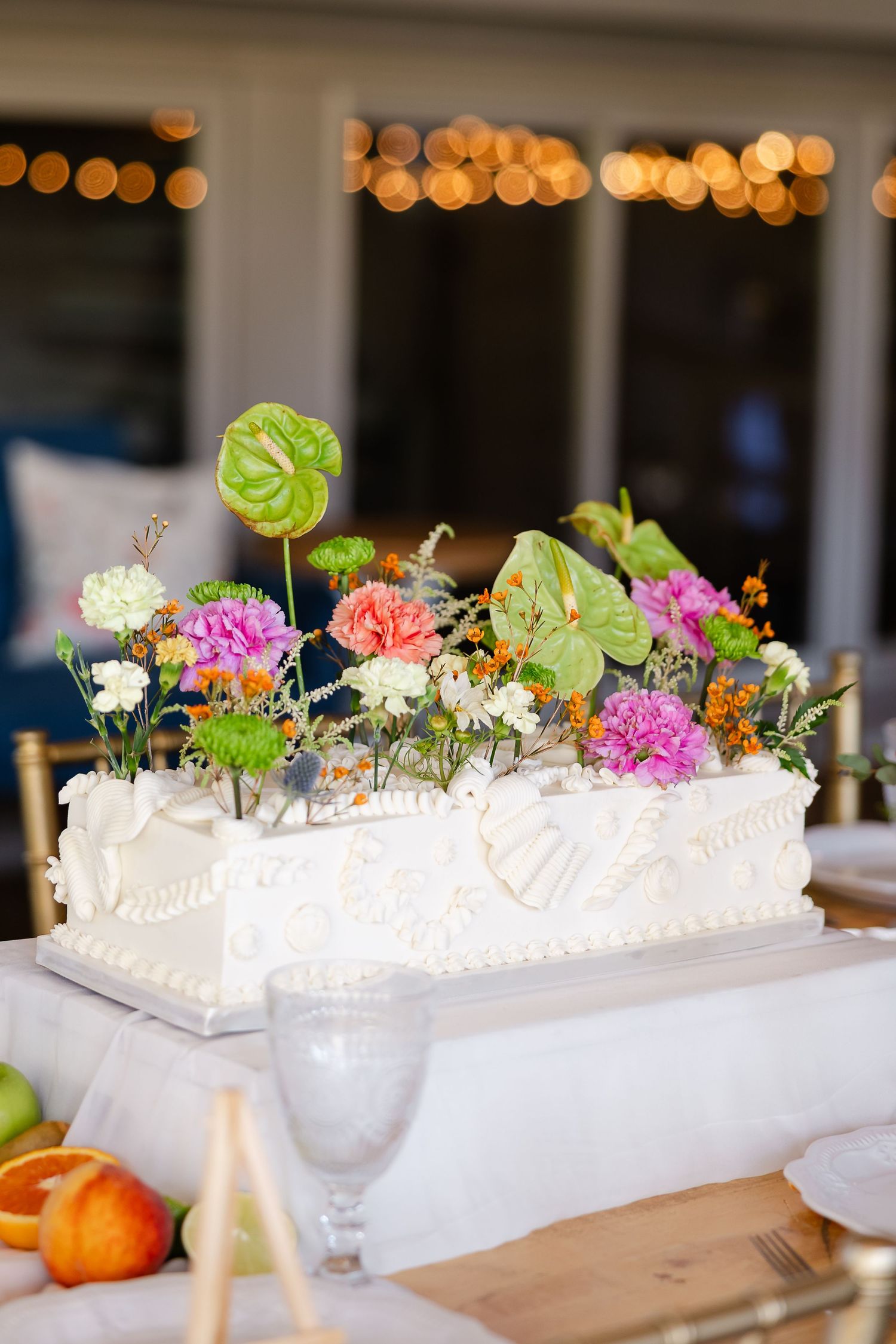 White sheet wedding cake topped with colorful fresh flowers including pink carnations and green anthuriums at a reception.At Drakewood Farms