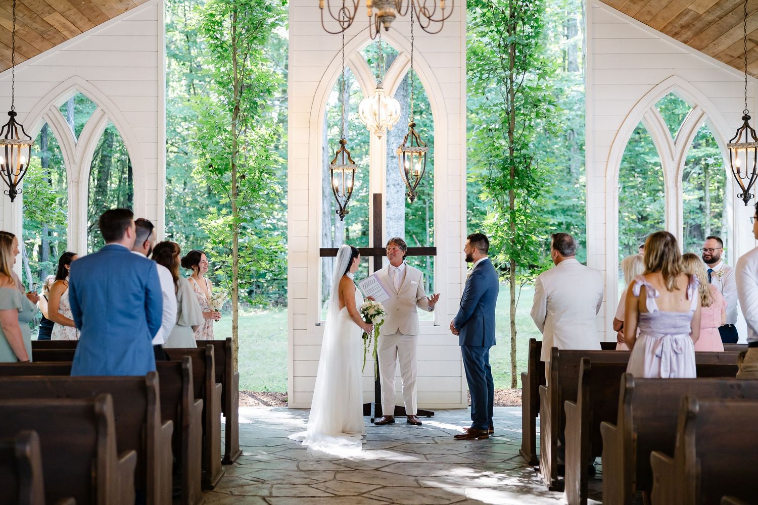Bride and groom exchange vows in a charming white chapel with gothic arched windows and elegant chandeliers. At firefly lane in Dickson, tn