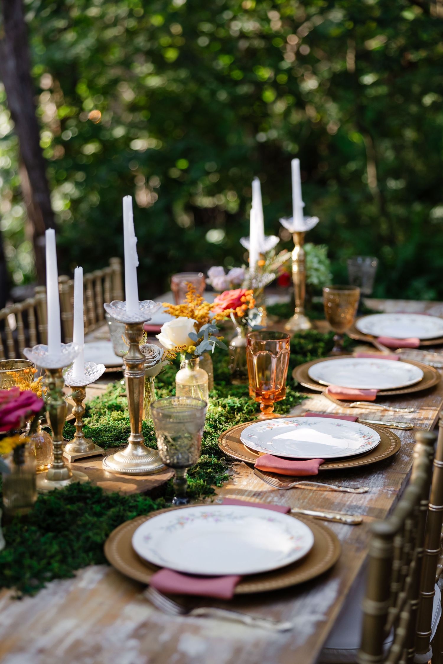 Elegant outdoor dining table with gold chargers, white candles, moss runner at Drakewood farms in Nashville, TN