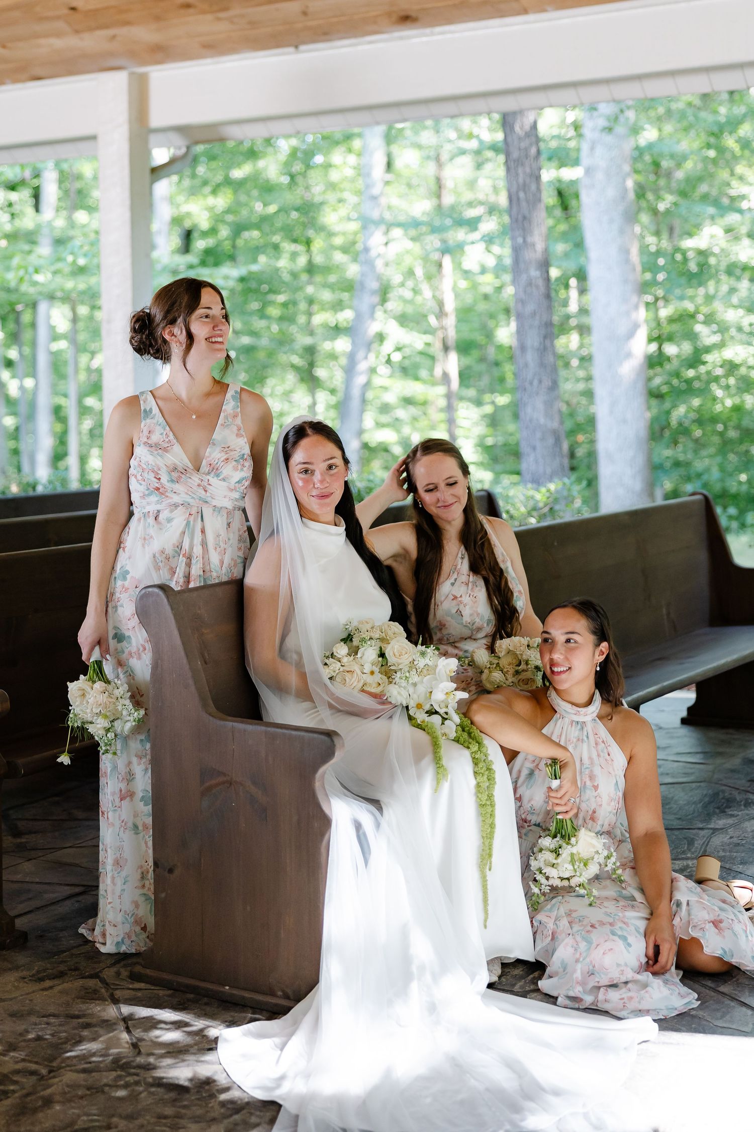 Bride in white gown sits in chapel pew surrounded by bridesmaids in floral dresses holding bouquets, At FireFly Lane in Dickson TN